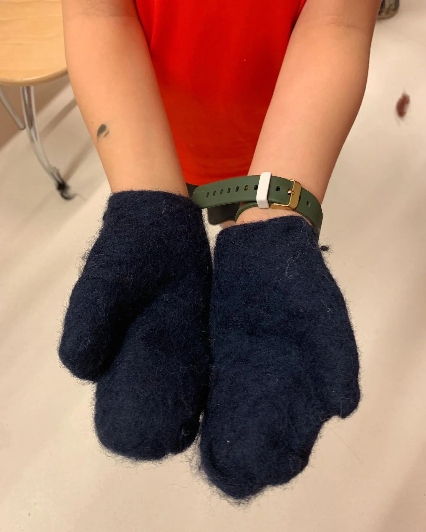 A person showing their arms with wool felted dark blue mittens on.