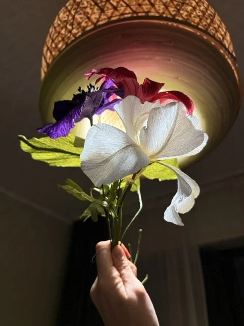 A hand holding a bouquet of artificial flowers with a large lampshade overhead.