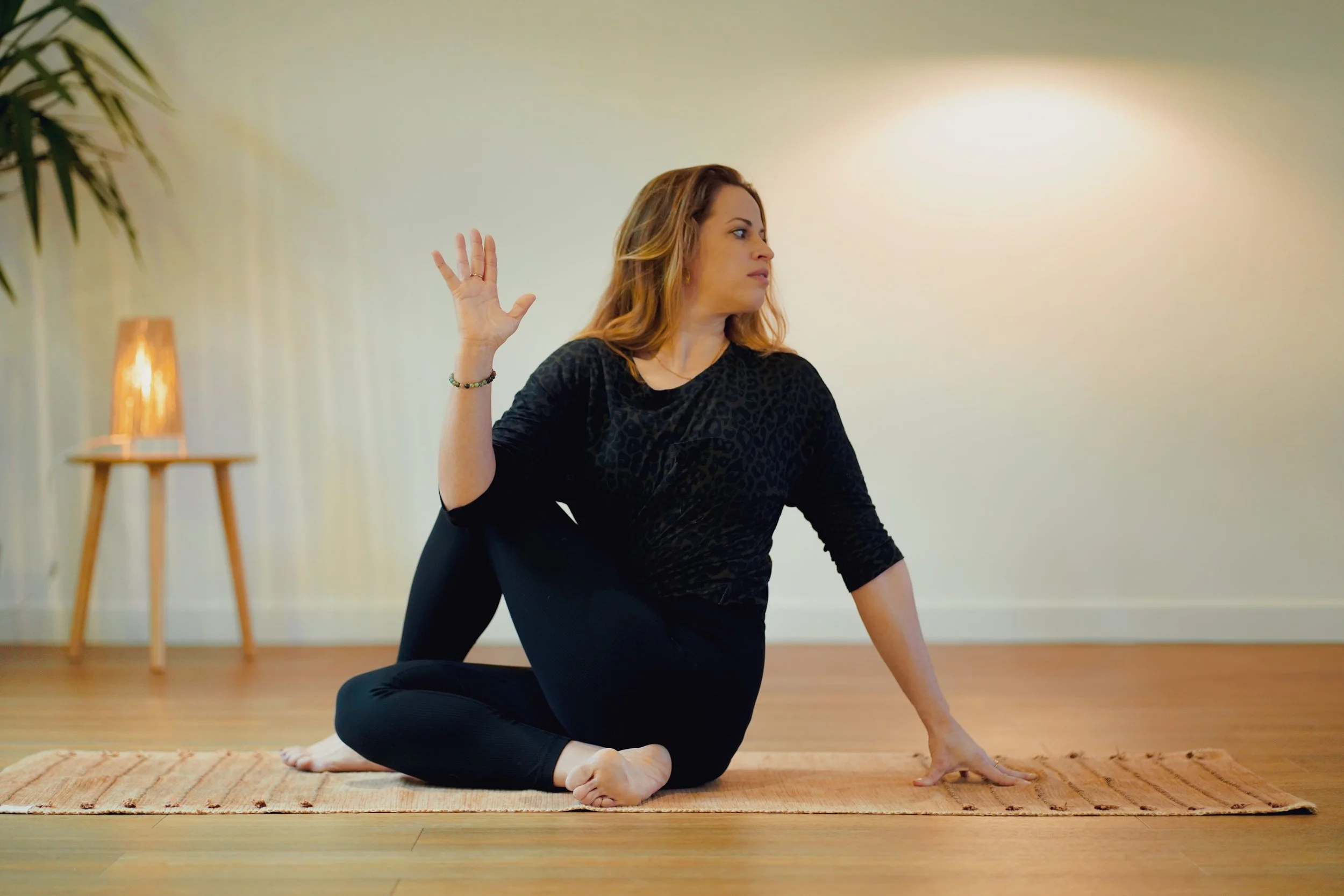Laura, professeure de yoga dans une posture sur un tapis, en levant la main droite et en regardant à gauche