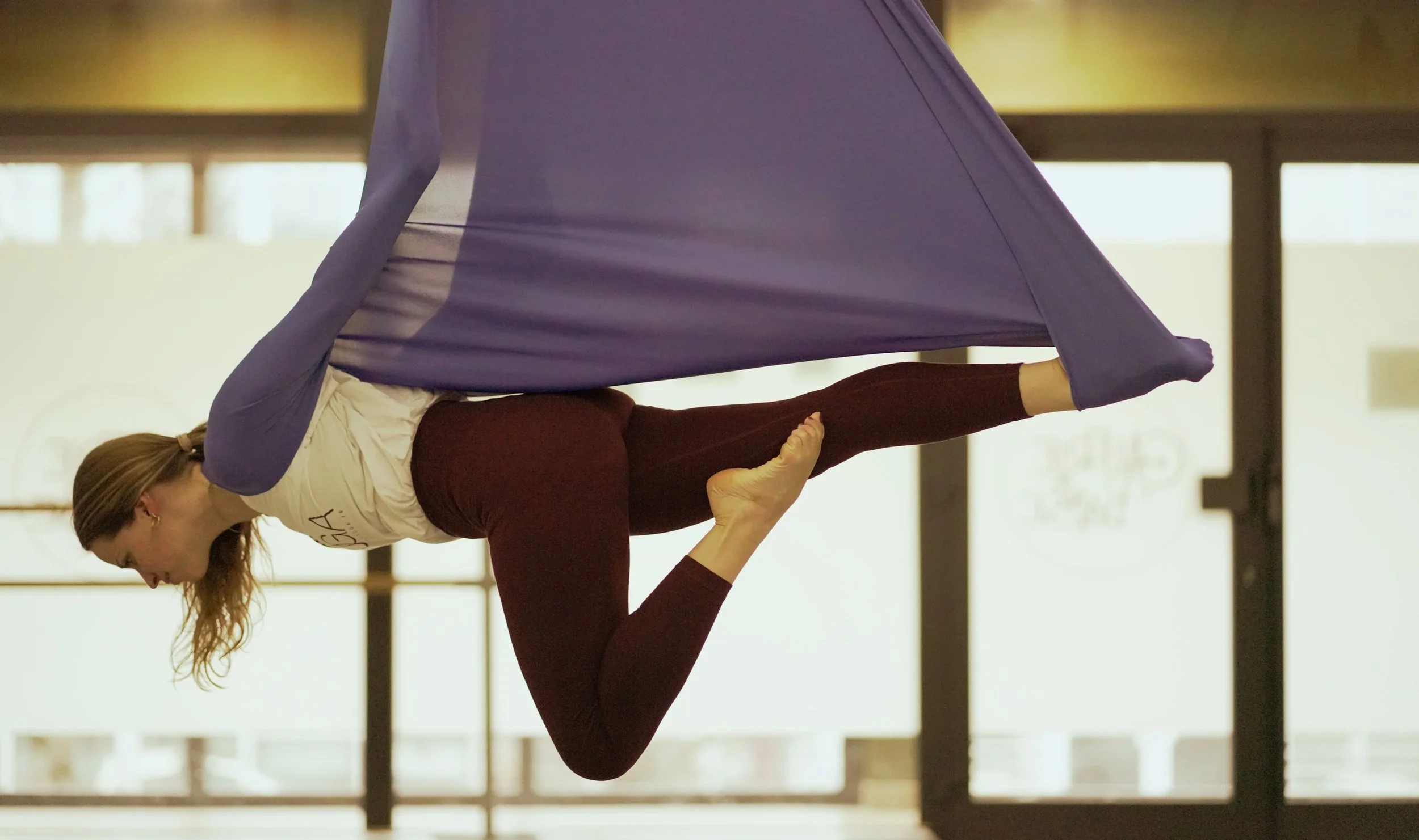 Deux femmes pratiquant le yoga dans un studio, dont une en position de balançoire sur l'autre.