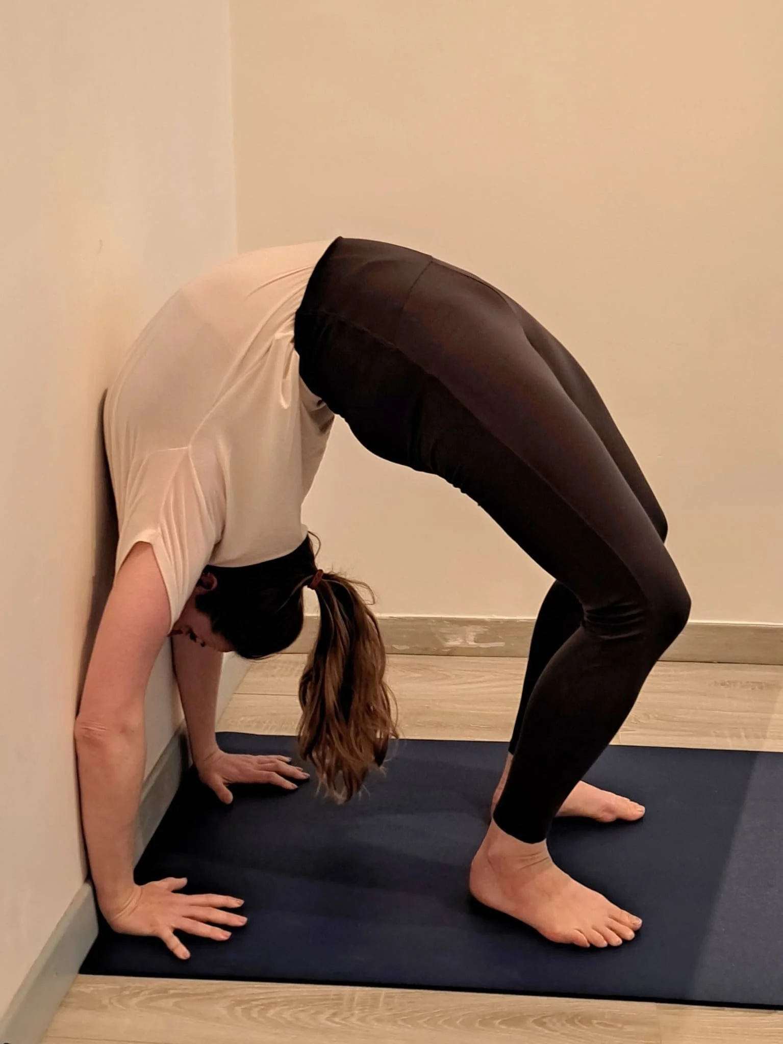 Une personne réalise une pose de yoga inversée contre un mur, en appui sur ses mains et ses pieds, formant un pont avec son corps.