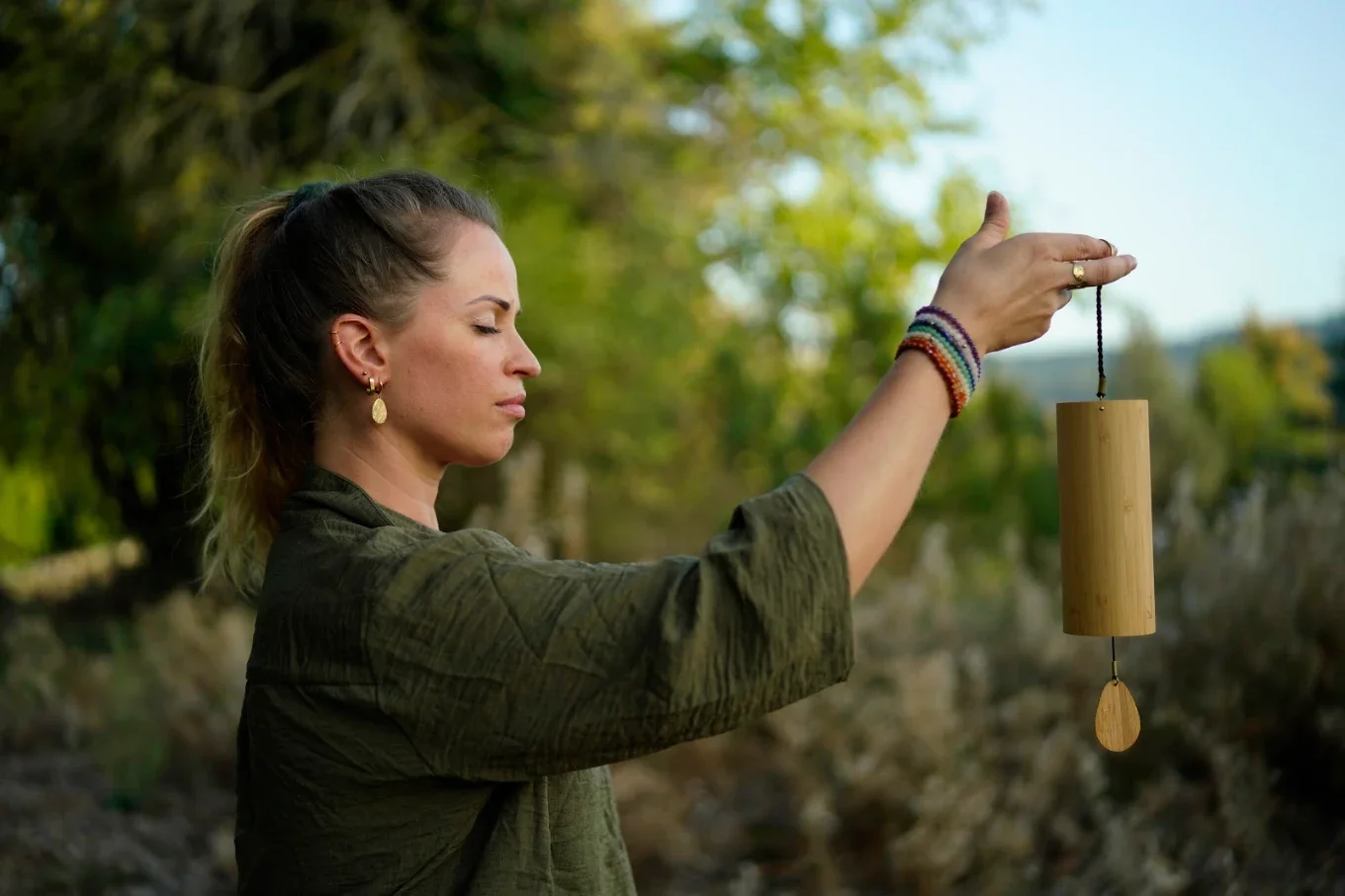 Laura, professeure de yoga tenant une cloche à vent en bois dans la nature