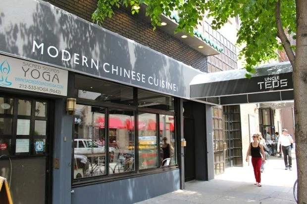 Exterior of a restaurant called Modern Chinese Cuisine with a black awning and windowed facade, on a city street with pedestrians and trees.