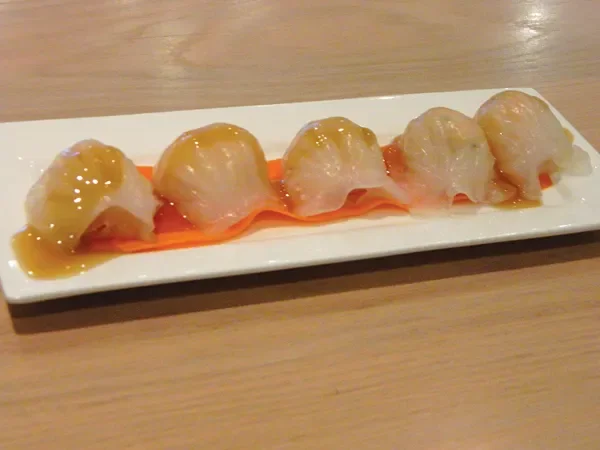 Six pieces of sushi with a golden sauce on top, served on a white rectangular plate with a garnish of sliced orange carrot.
