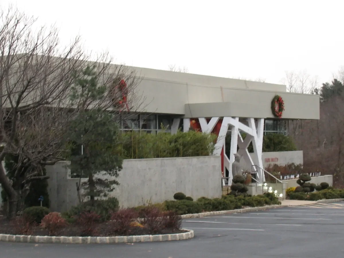 Building decorated with Christmas wreaths, surrounded by trees and shrubs, with parking lot in the foreground.