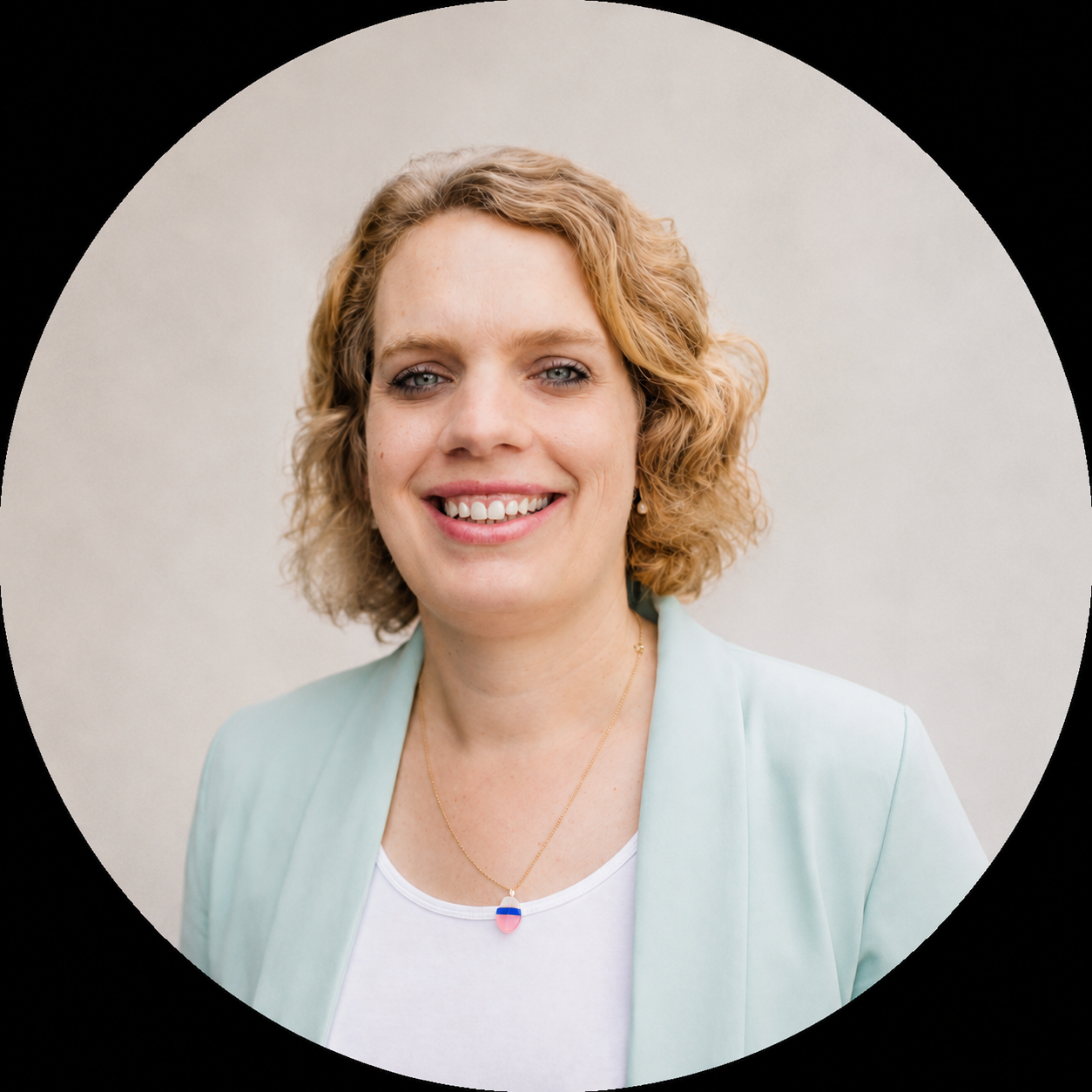 Porträt von Dr. Meike Hilgemann mit lockigem, blondem Haar. Sie trägt einen türkisfarbenen Blazer, ein weißes Top und eine Halskette mit einem halb Rosinen, halb blauen Anhänger. Der Hintergrund ist neutral.