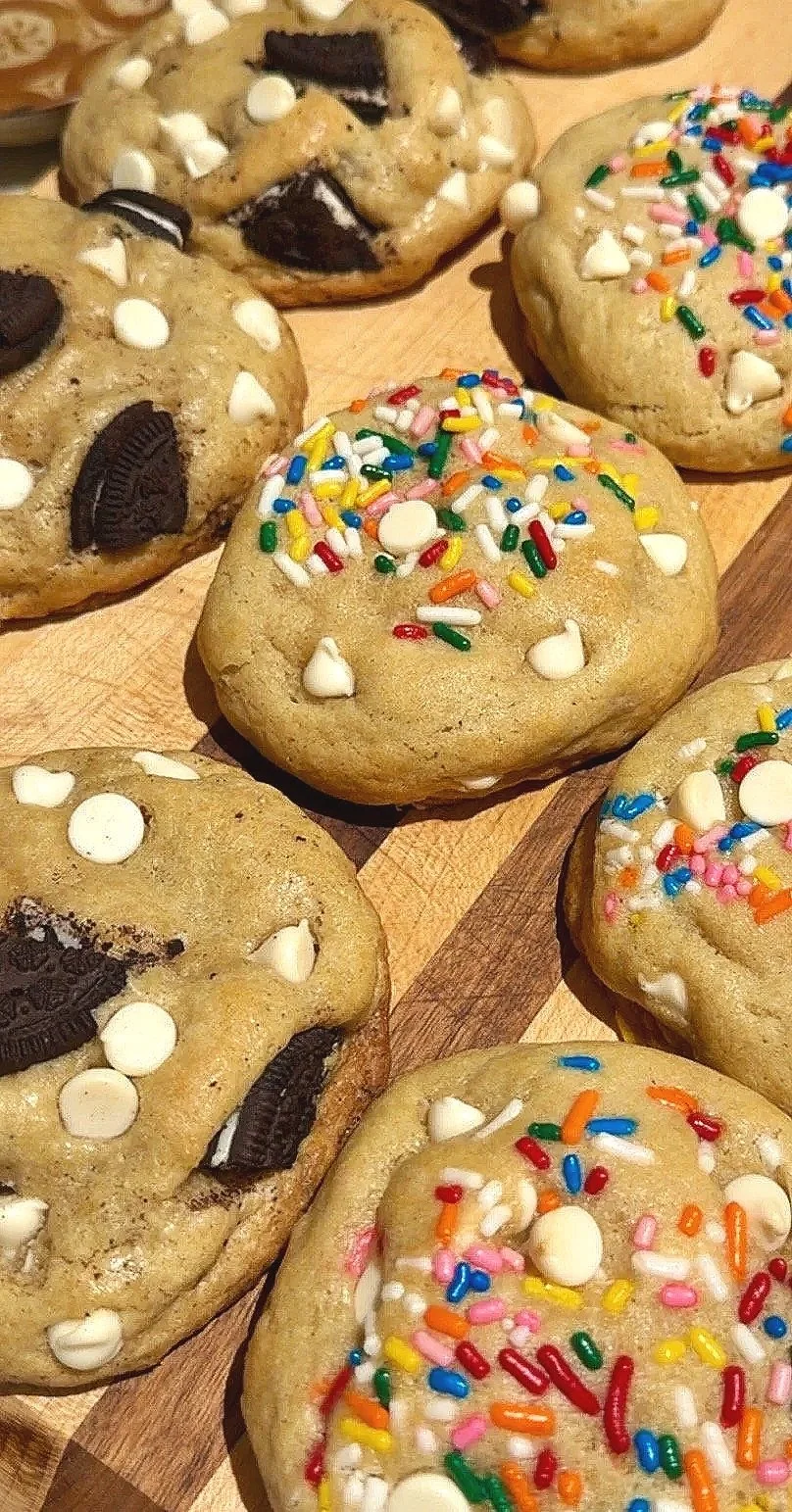 Group of cookies, some decorated with colorful sprinkles and white chocolate chips, others with Oreo cookies and white chocolate chips.