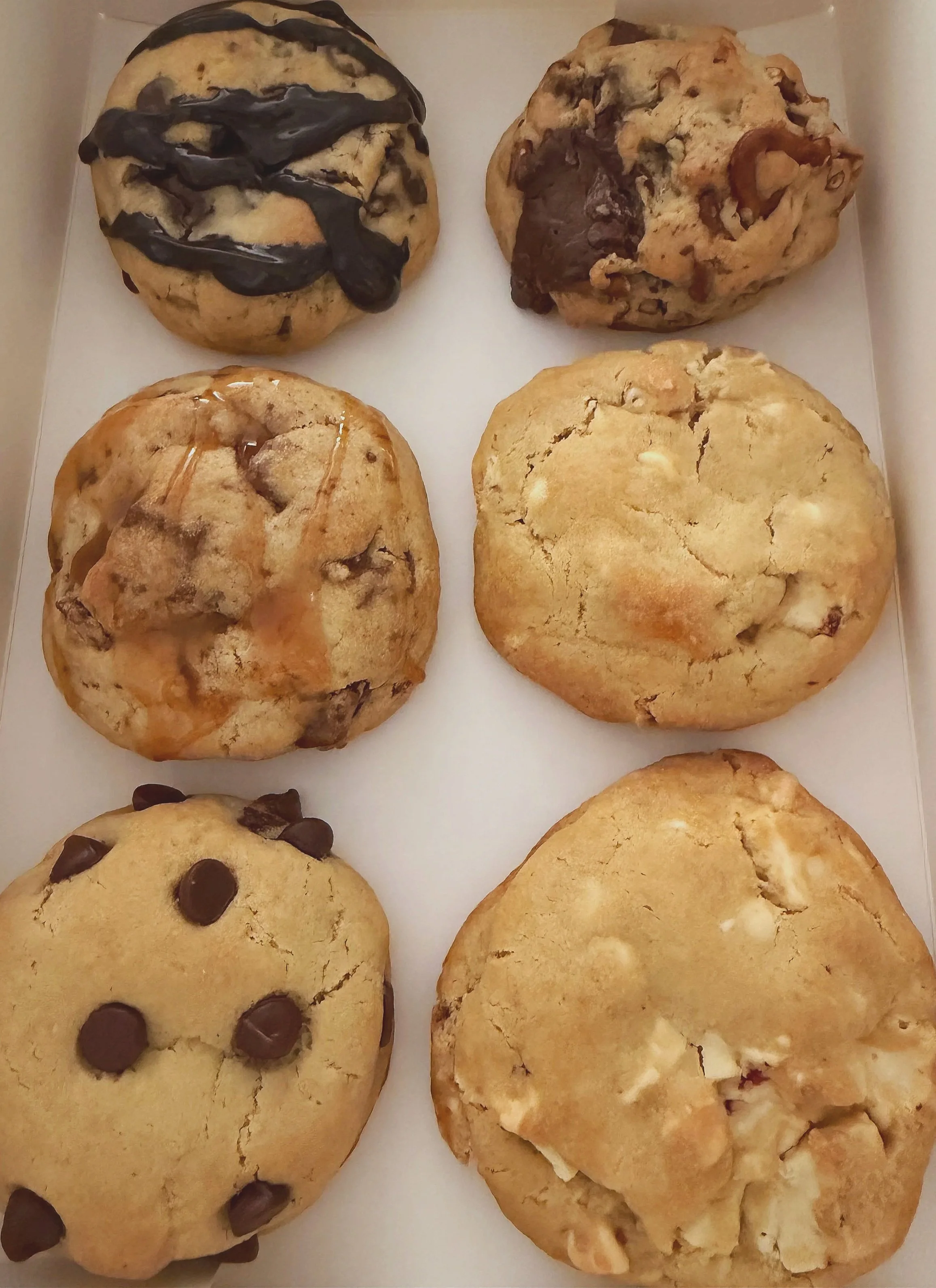 Six large cookies in a box, including chocolate chip, chocolate, and other varieties.