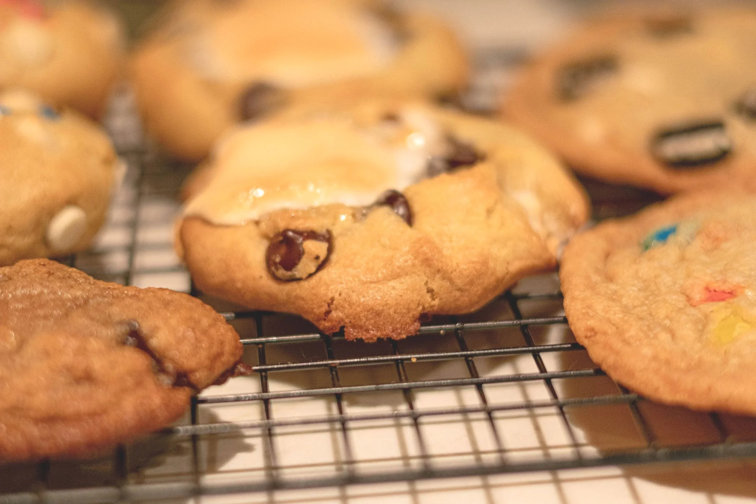 Close-up of freshly baked cookies on a cooling rack, including chocolate chip and birthday cake cookies.