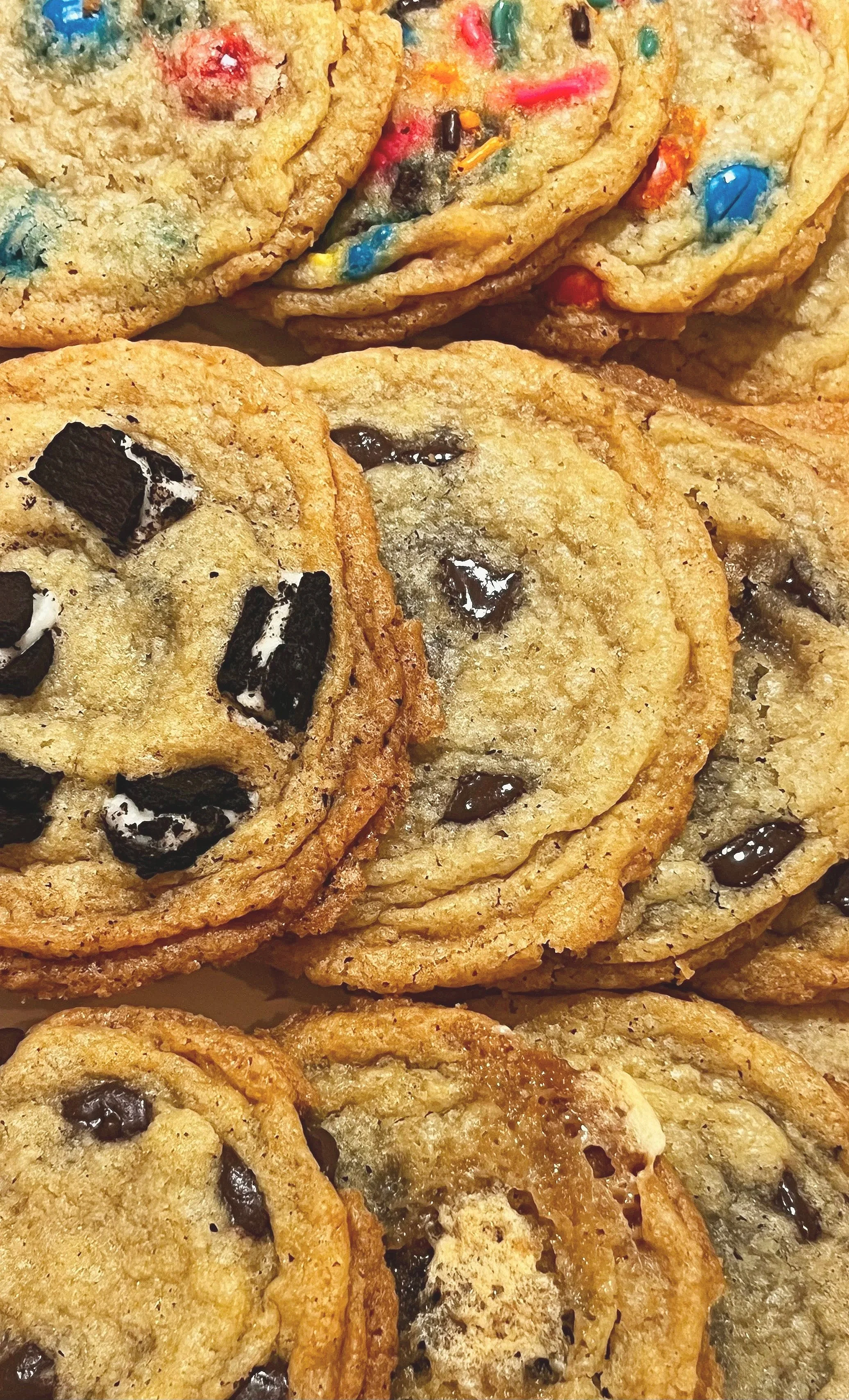 Close-up of stacked chocolate chip cookies with colorful sprinkles, Oreo cookies, and cookie dough with candy pieces.