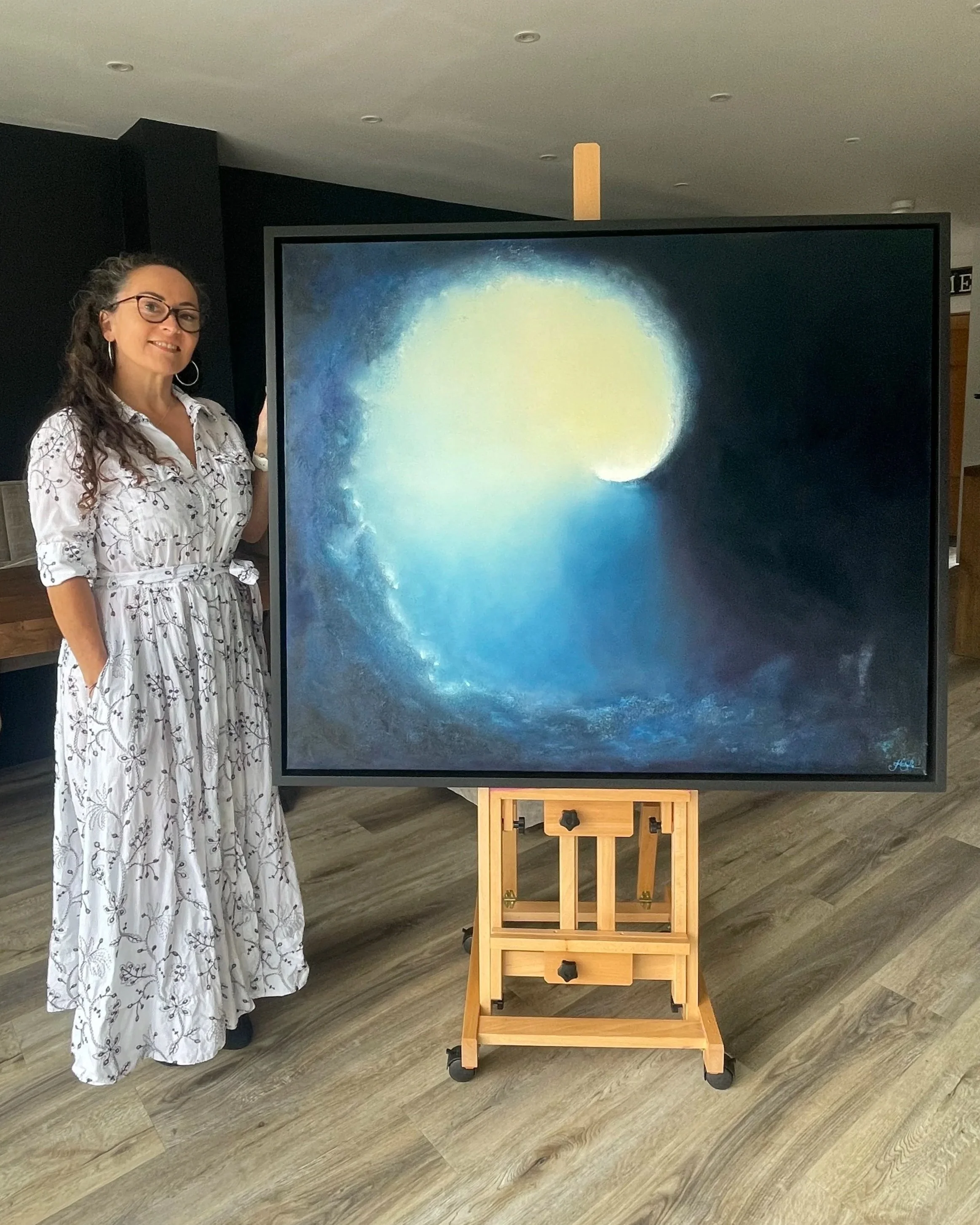 Artist Mechelle Tebbs standing beside her atmospheric abstract oil painting, Emergence.