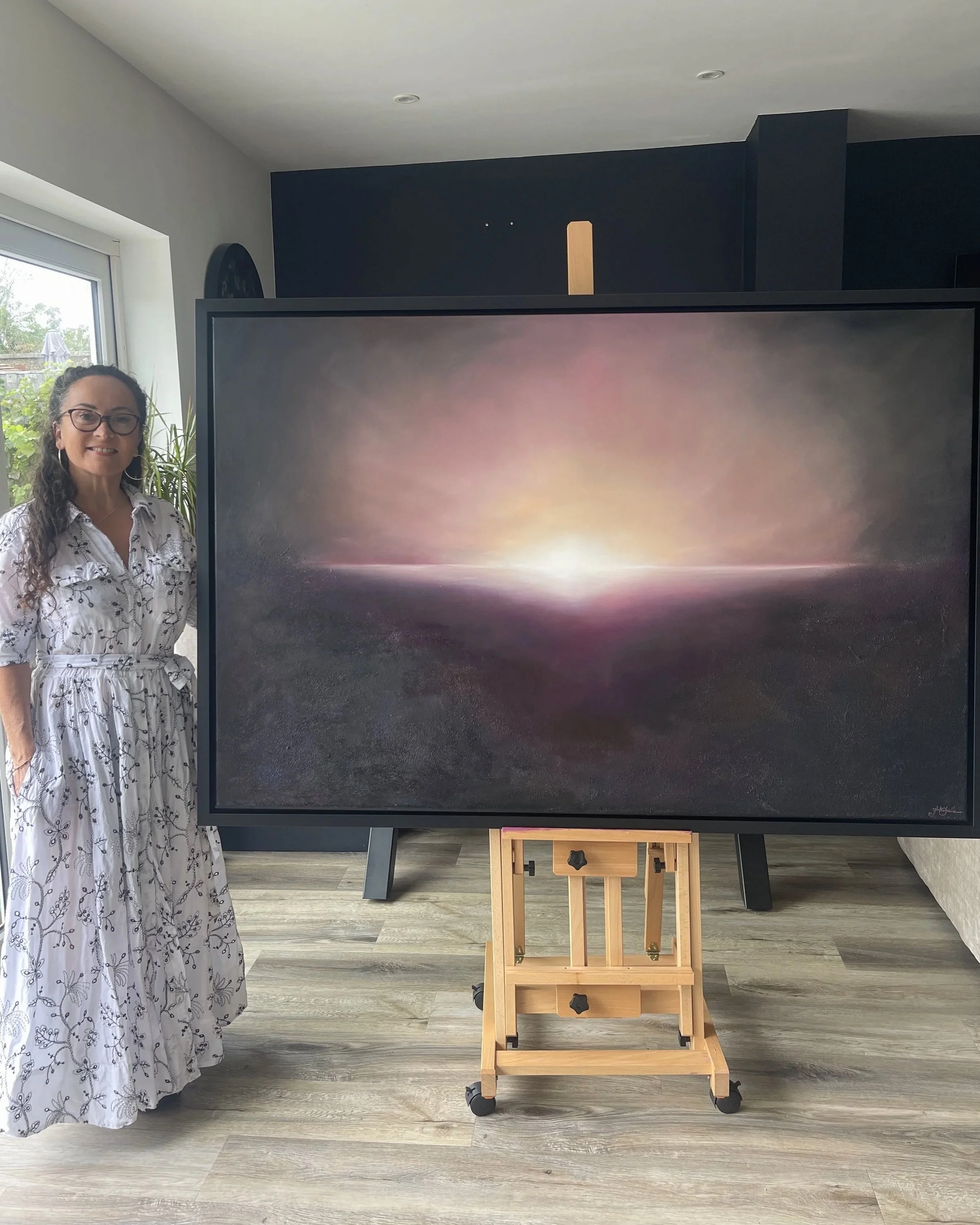Artist Mechelle Tebbs standing beside her atmospheric abstract oil painting, Coming Home.