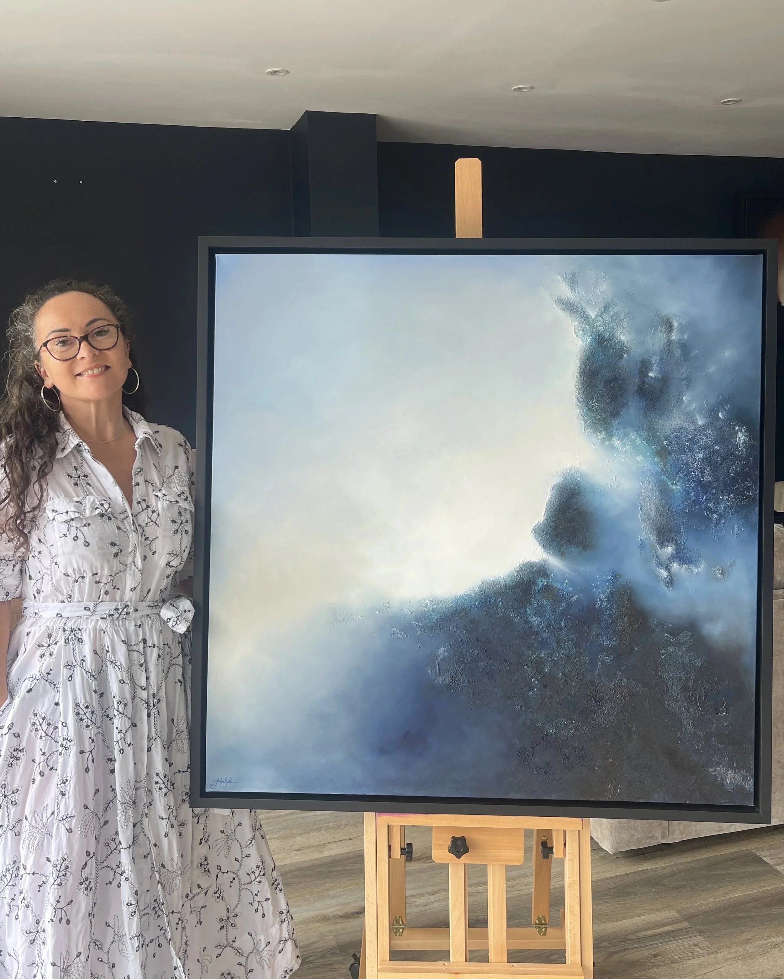 Artist Mechelle Tebbs standing beside her blue atmospheric abstract oil painting, Sanctuary.