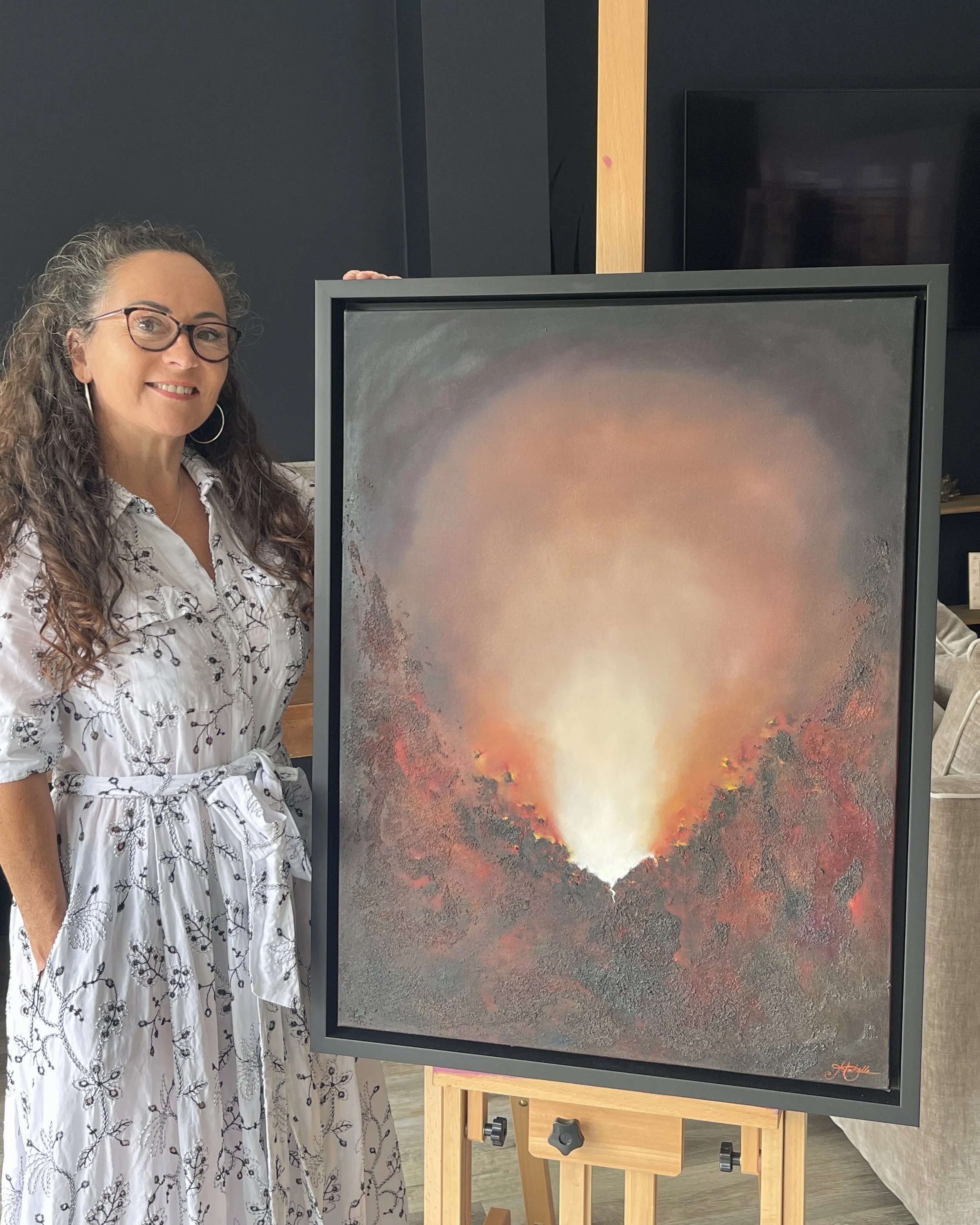 Artist Mechelle Tebbs standing beside her atmospheric abstract oil painting, Unextinguished.