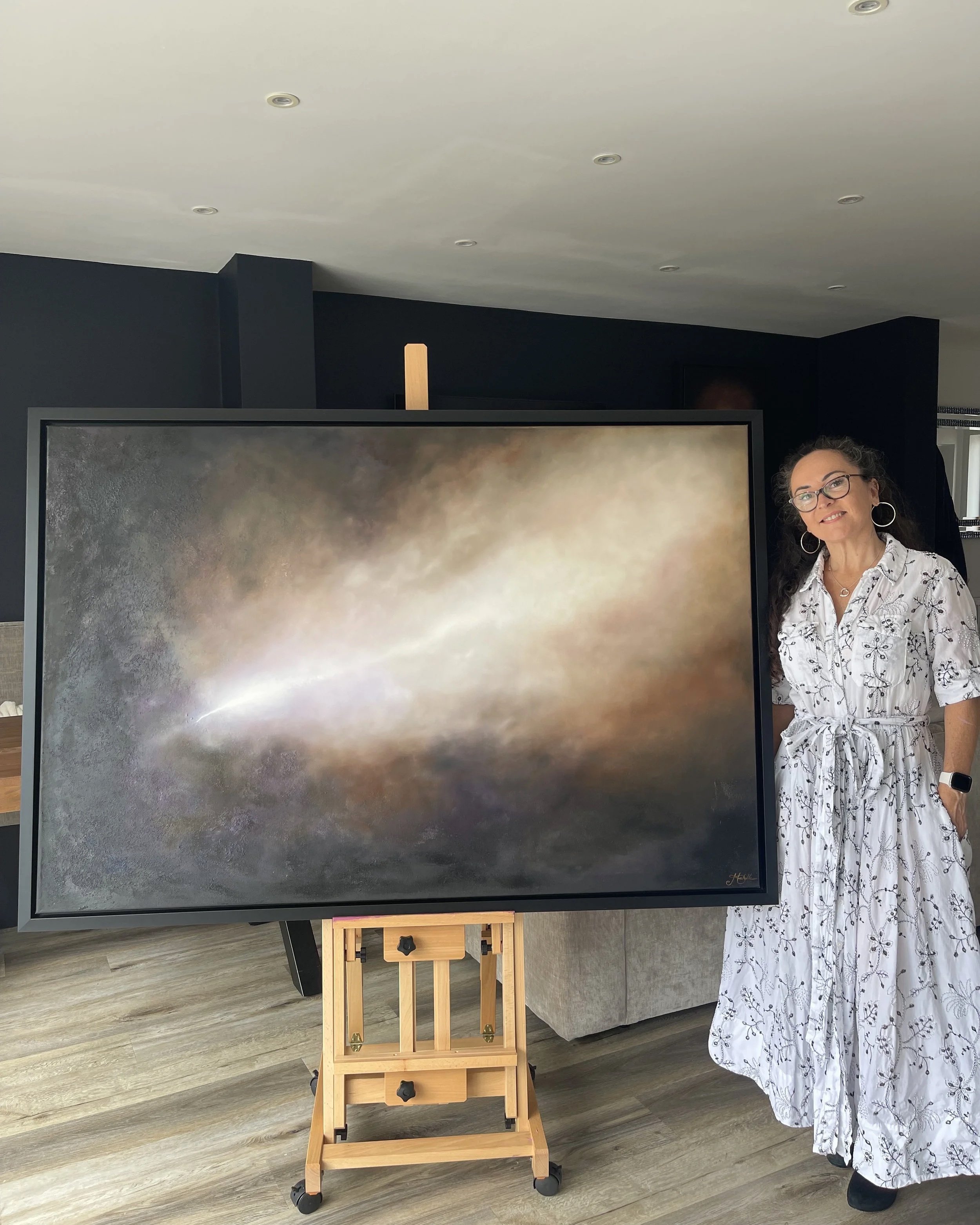 Artist Mechelle Tebbs standing beside her atmospheric abstract oil painting, Awakening.