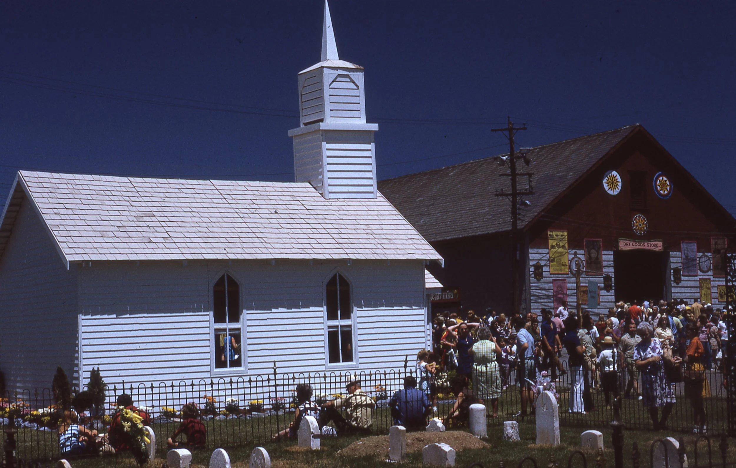 Replica church building and graveyard on Festival grounds, surrounded by crowd of Festival attendees.