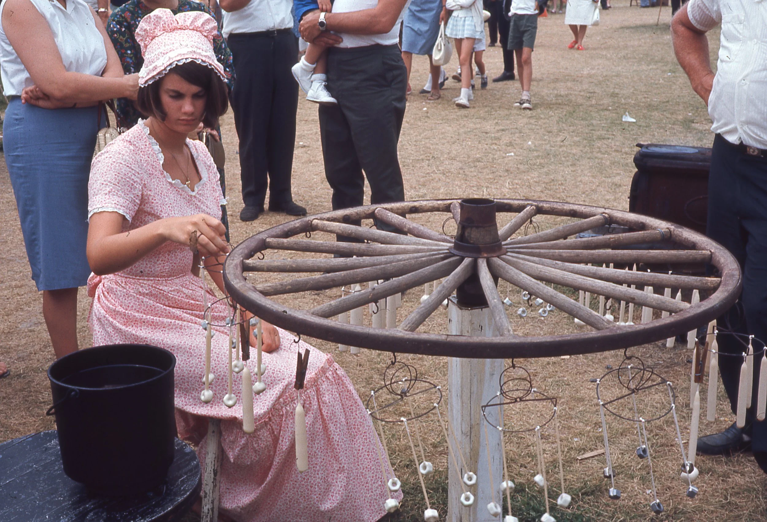 Woman in long dress and bonnet hanging hand-dipped candles on wheel-shaped wooden frame.