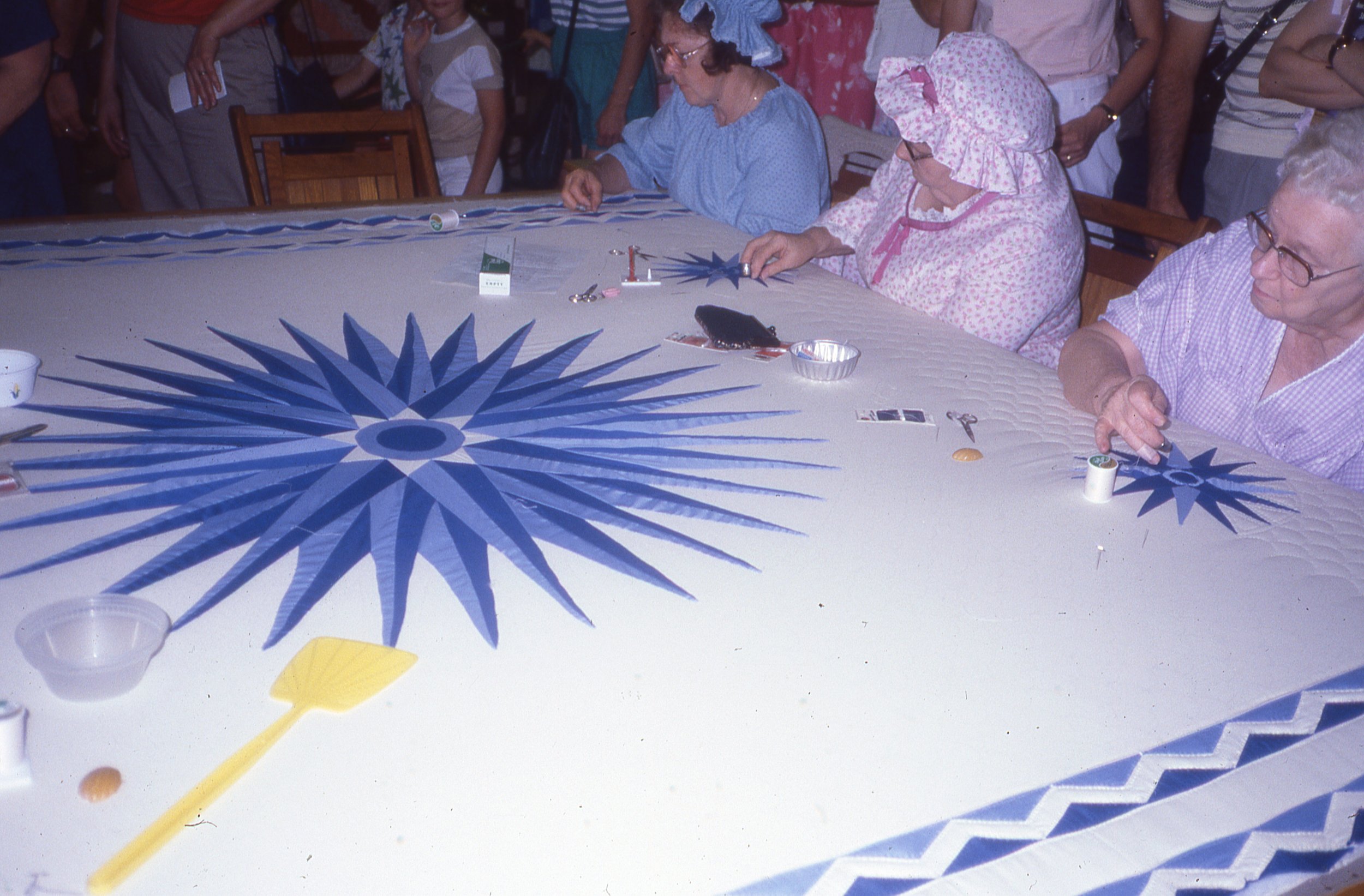 Three women hand-sewing large quilt for audience.
