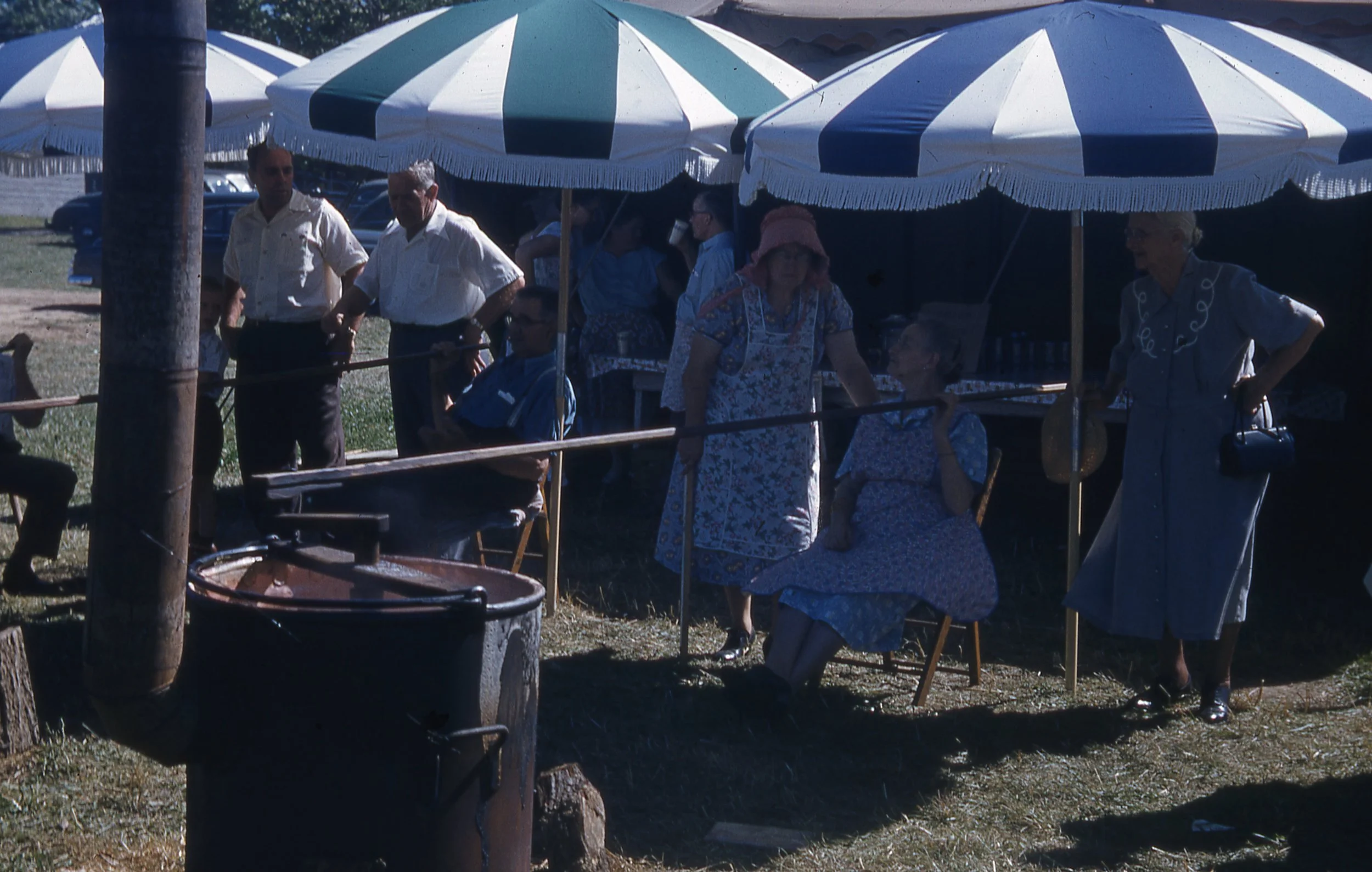 Man and woman stirring two large kettles of cooking apple butter.