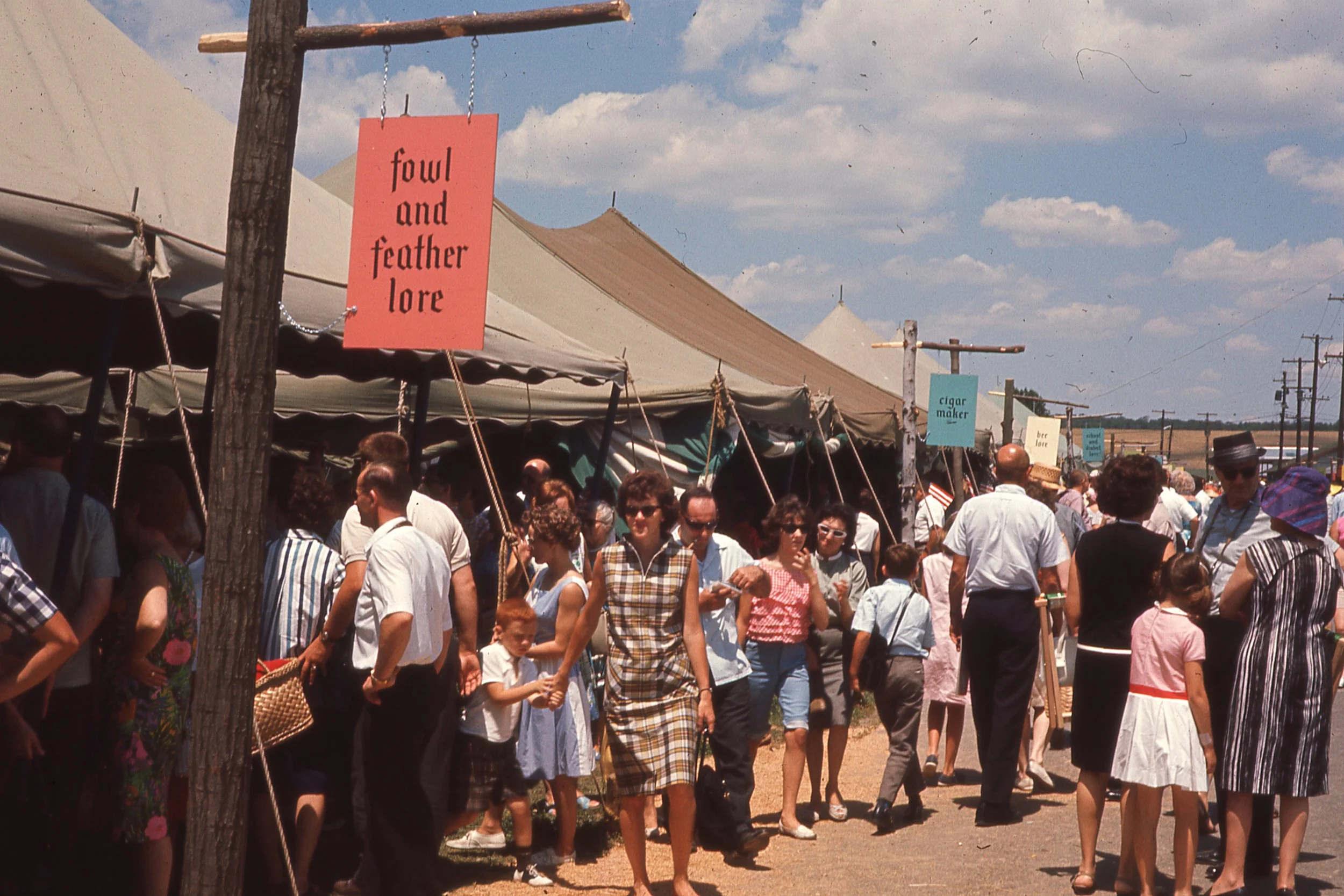 Crowd walking along line of tents on Festival grounds. 
