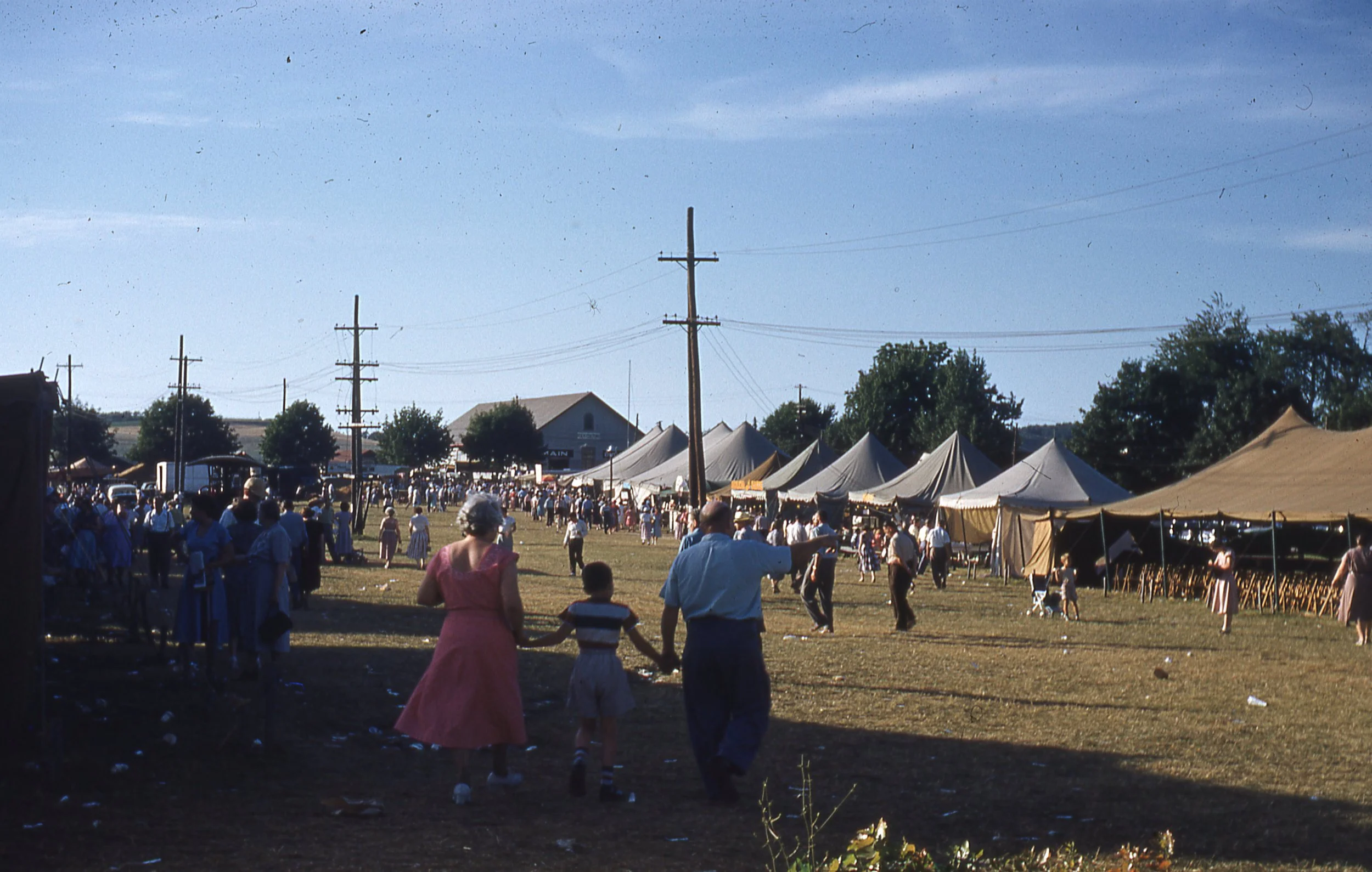 Row of tents and and crowd on wide grass walkway on Festival grounds.