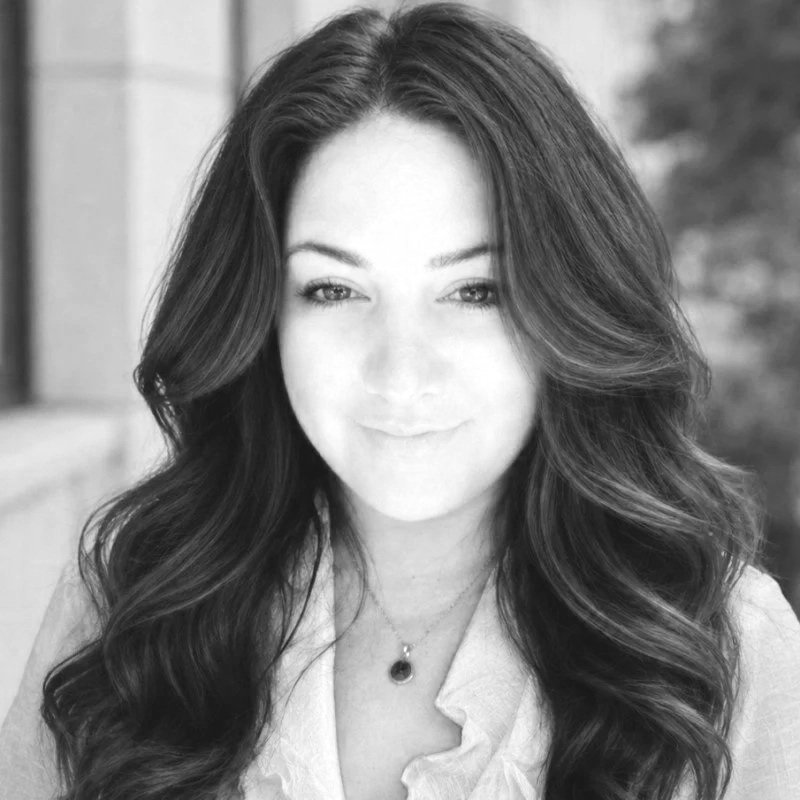 A woman with long, wavy hair and a gentle smile, wearing a light-colored top and a necklace, in black and white.