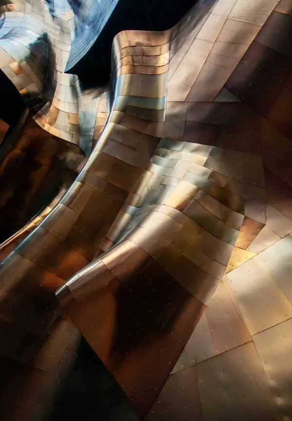 Abstracte metalen architectuur met golvende en gekantelde oppervlakken, reflecterend licht en donkere tinten.