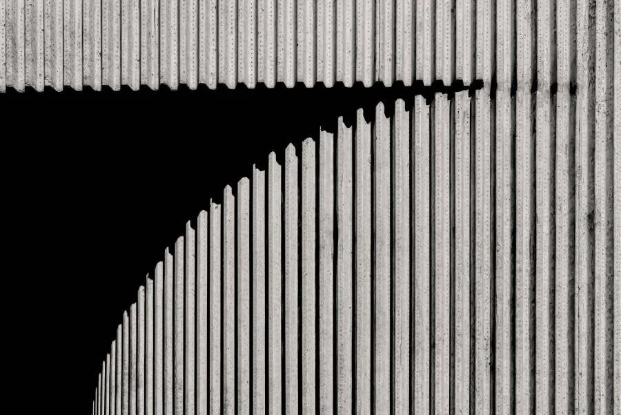 Een close-up van een betonnen muur met verticale groeven en een schaduw die een hoek creëert.