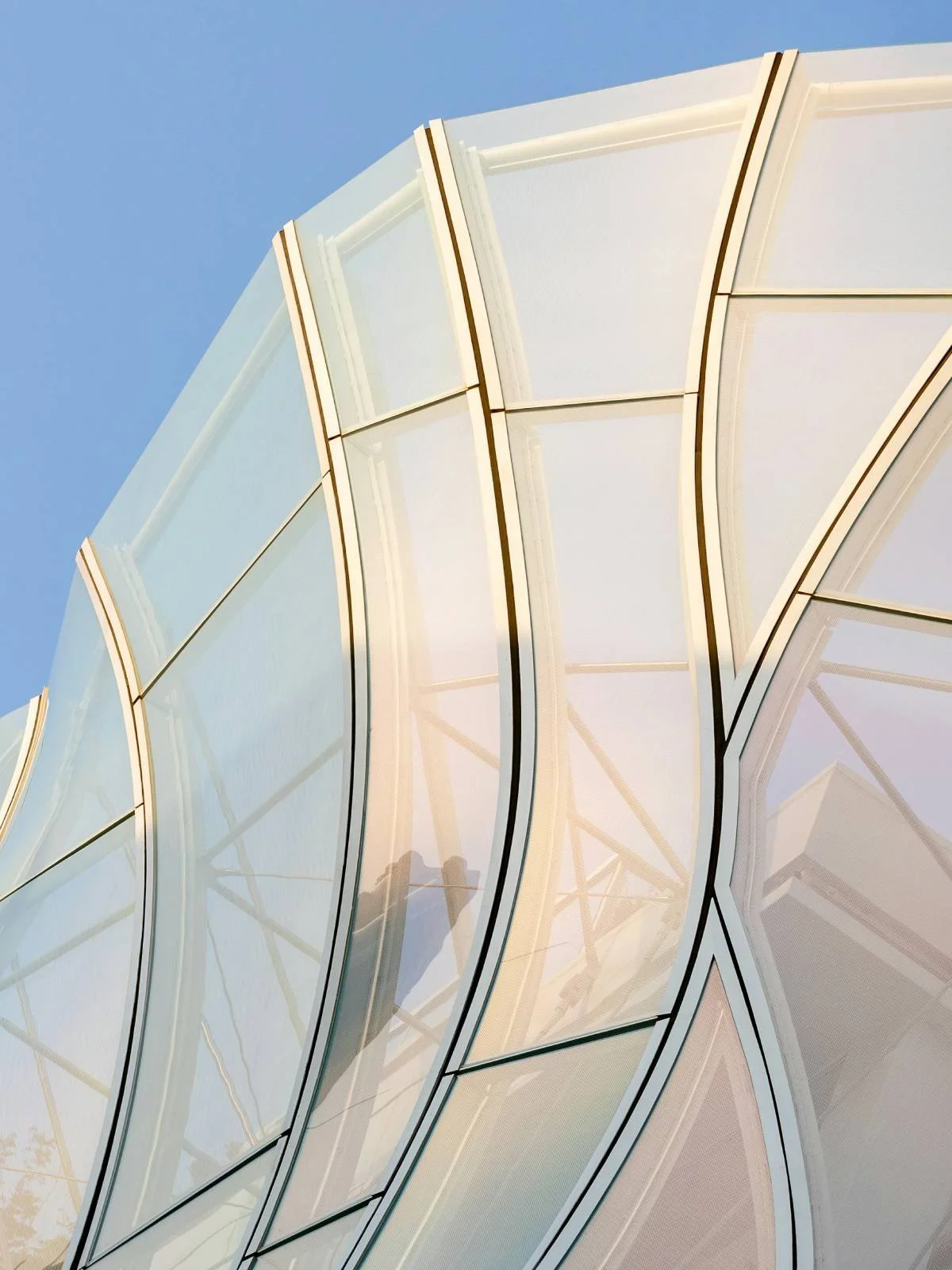 Een moderne glazen en metalen architectuur met vloeiende lijnen tegen een blauwe hemel.