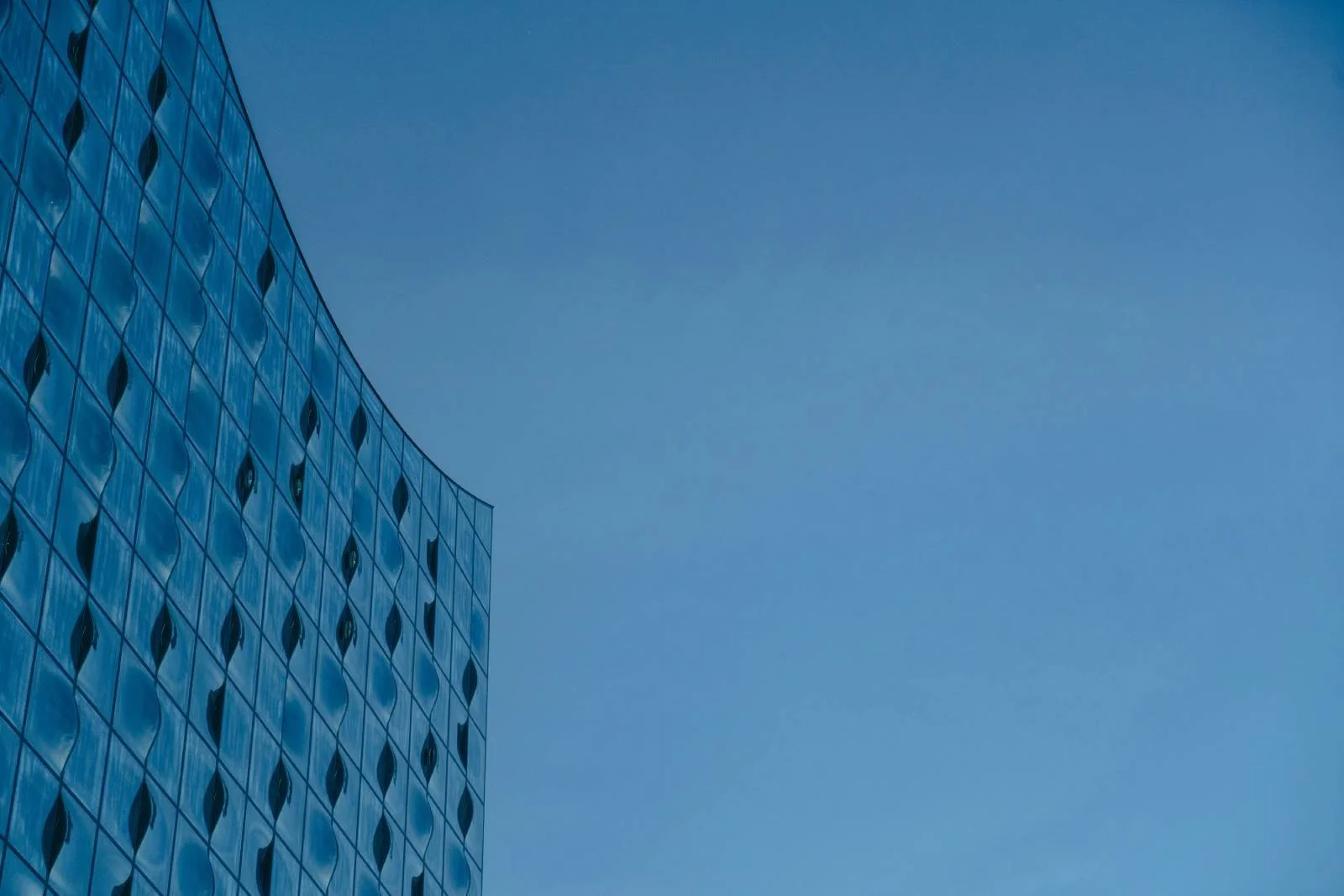 Een moderne glazen kantoorgebouw met een golvende gevel tegen een heldere blauwe lucht.