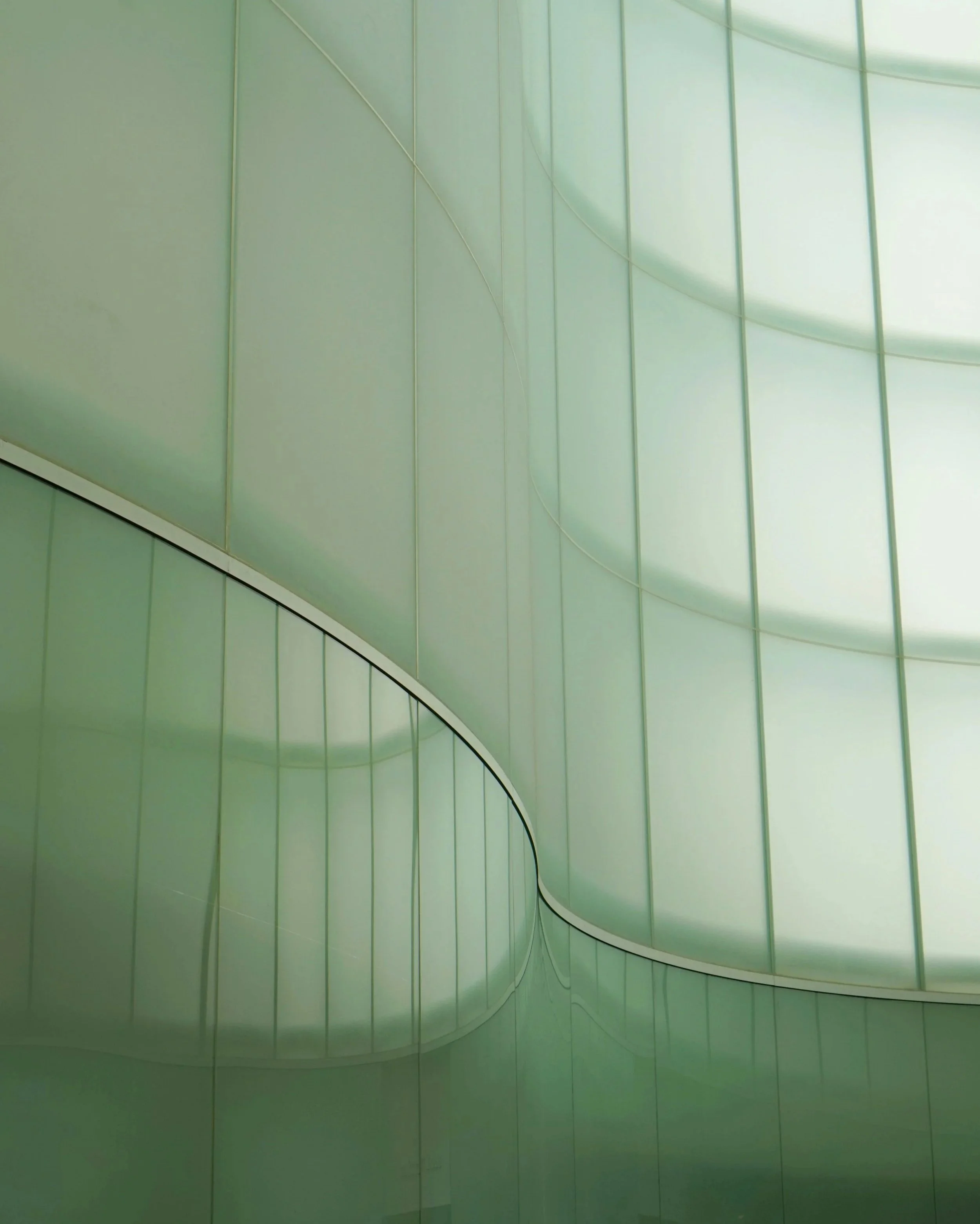 Close-up van een modern gebouw met groene glazen ramen en een boogvormig ontwerp.