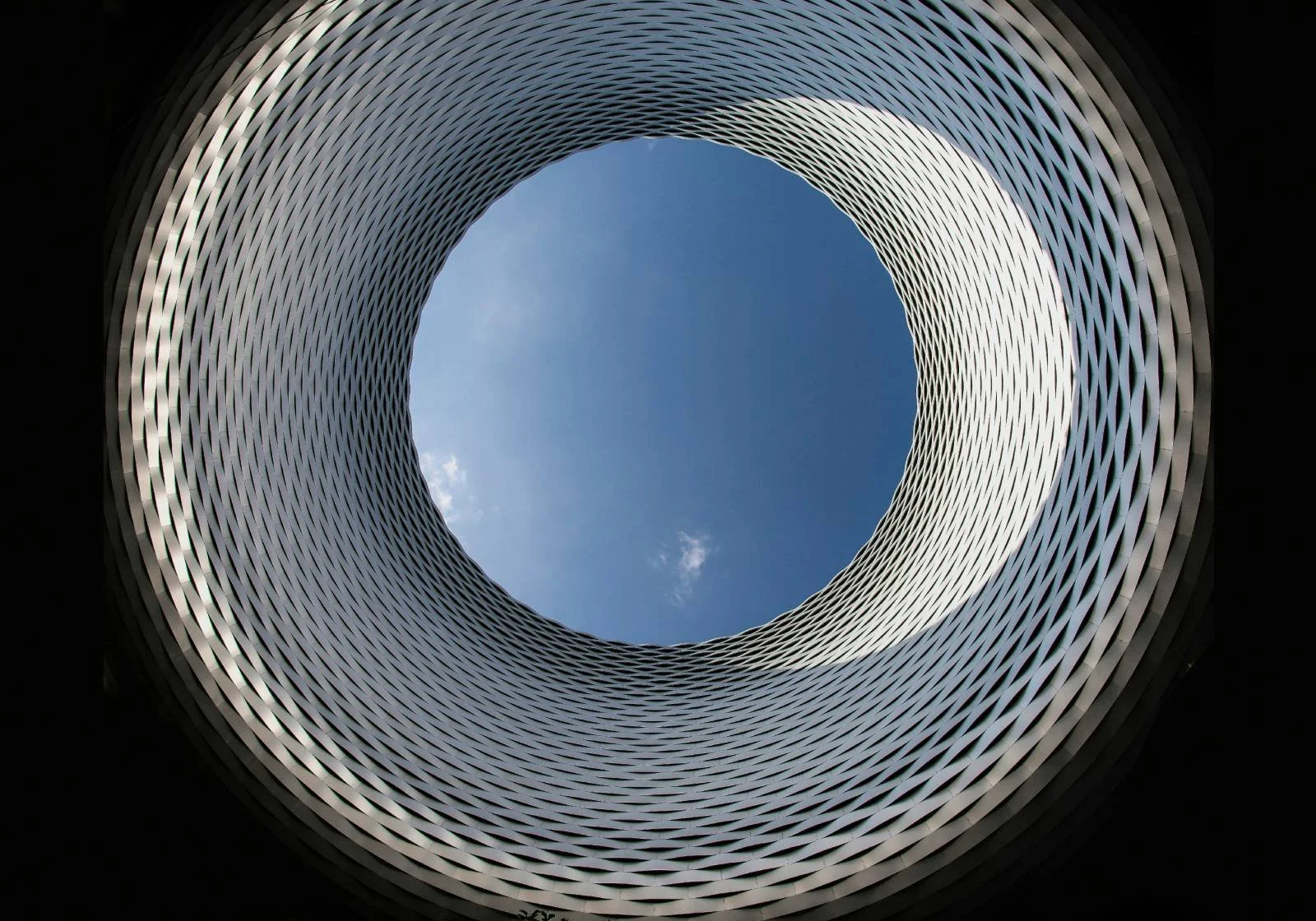 Binnen in een modern, cylindrisch gebouw met een open dak, uitzicht op de blauwe hemel en wolken.