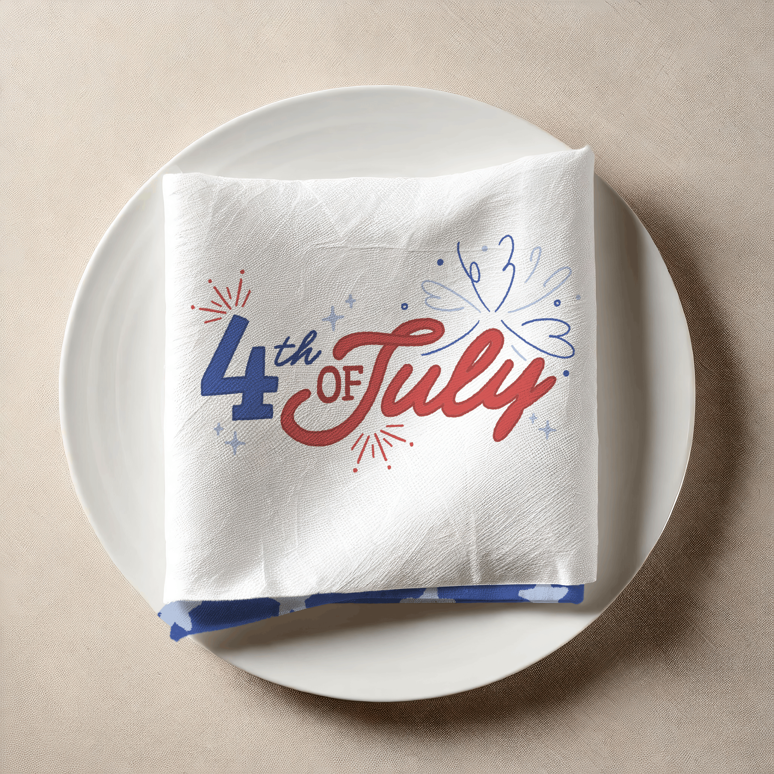 Close-up of a white plate with a decorated napkin or paper towel that reads "Happy 4th of July" with red, white, and blue fireworks and stars, set against a beige and brown background.