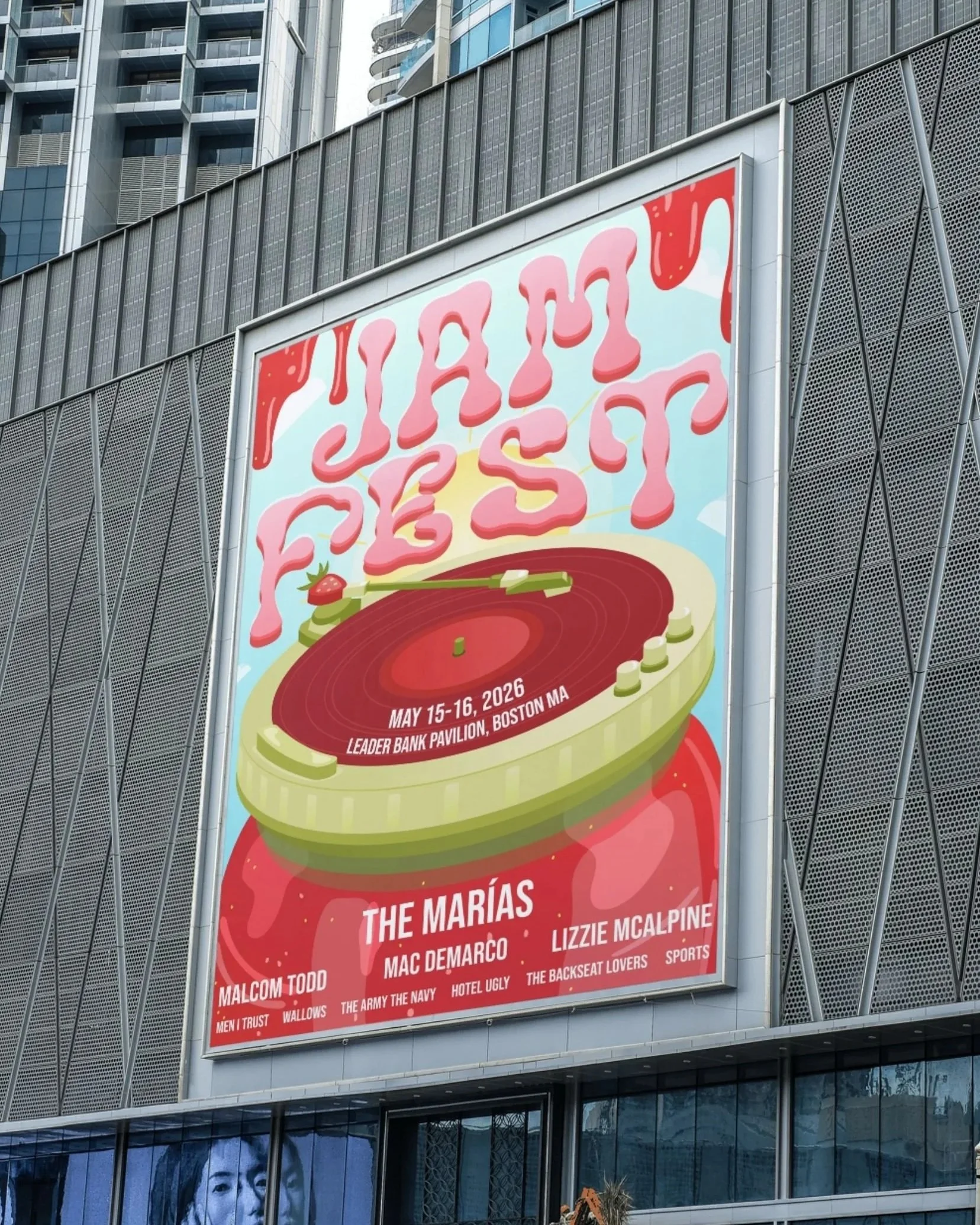 Large red billboard on a modern building advertising a 2026 music indie festival called 'Jam Fest.' The billboard features a graphic of a jam jar turntable and text with event dates, at the Leader Bank Pavilion in Boston, Massachusetts.