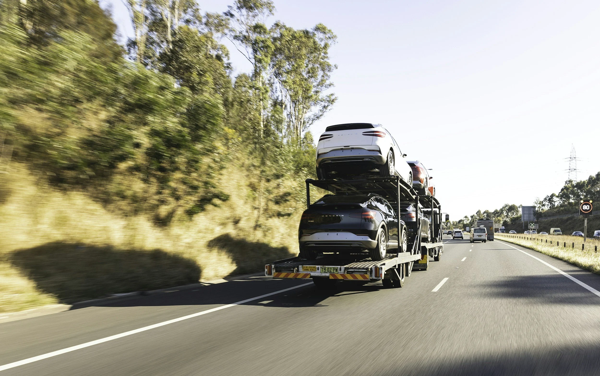 A car carrier truck driving on a highway with cars loaded on the trailer, surrounded by trees and other vehicles.
