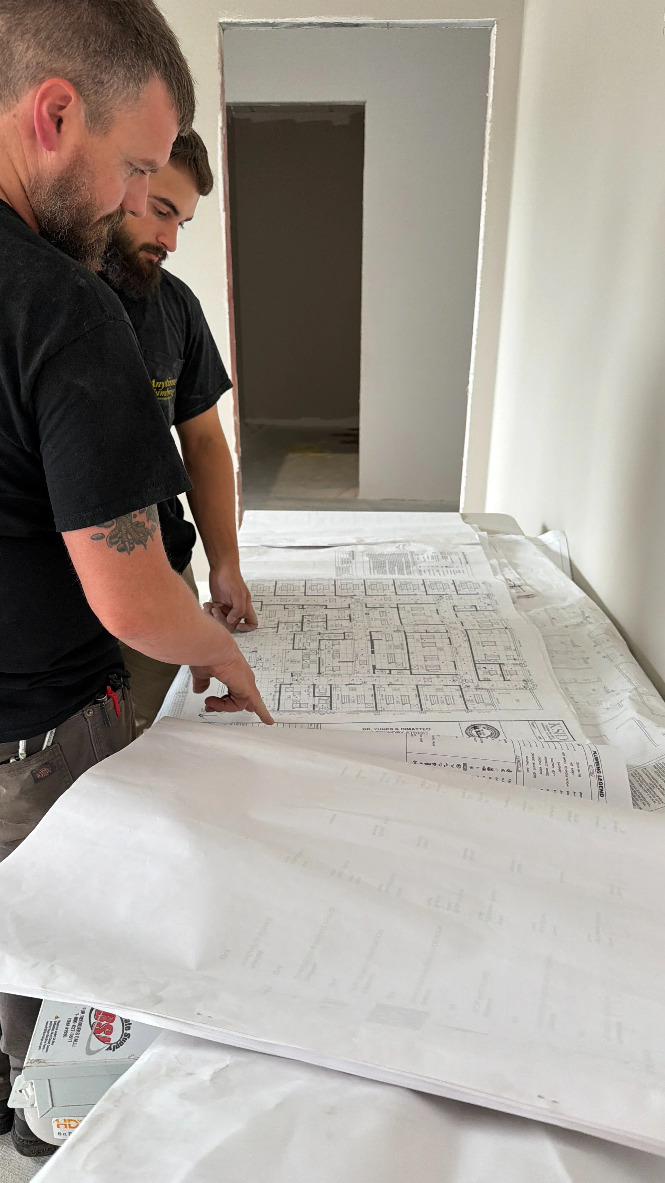 Two men examining architectural blueprints on a table in a construction or renovation site.