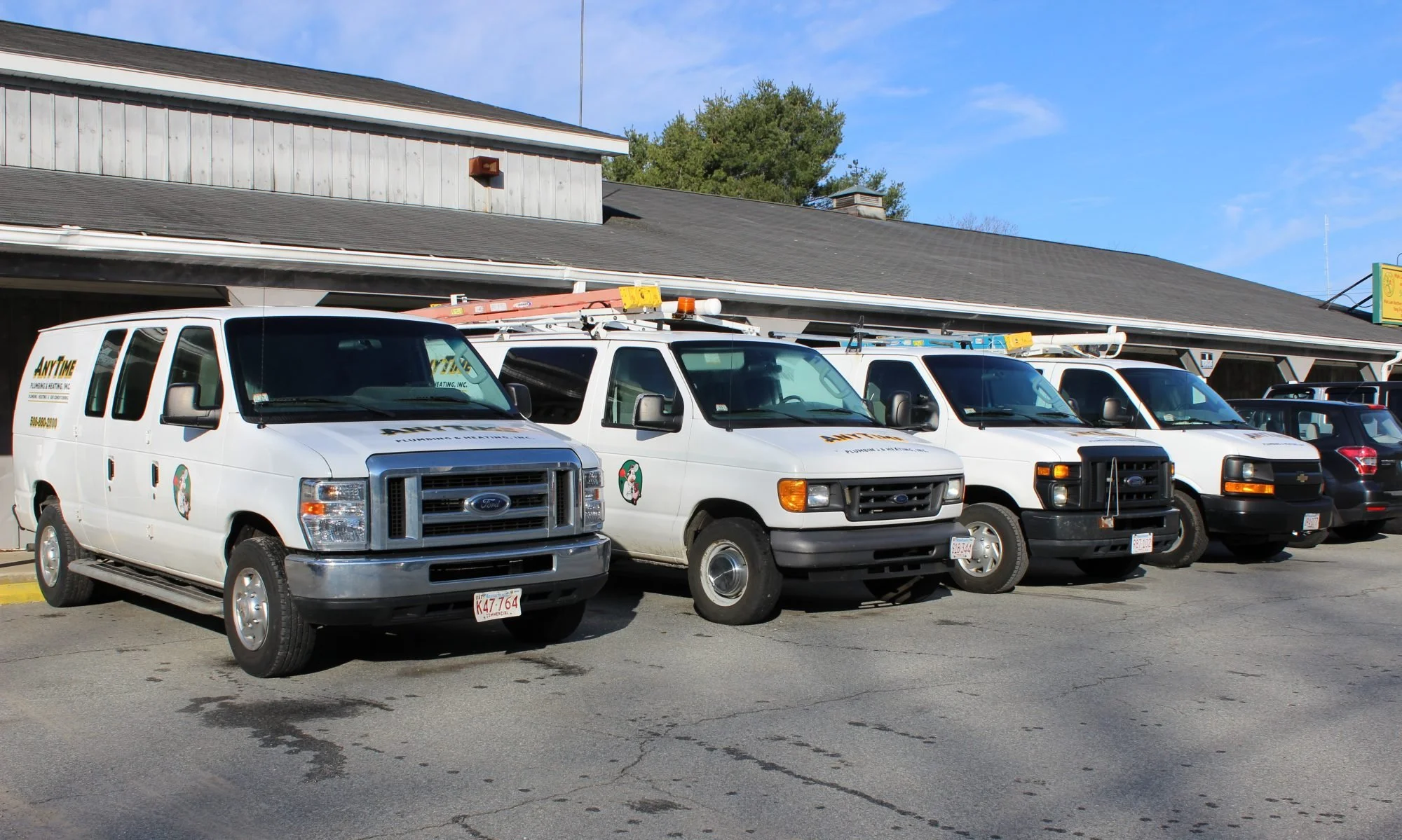 Pickup trucks parked in front of a building, with a ladder and equipment on top, under a clear blue sky.