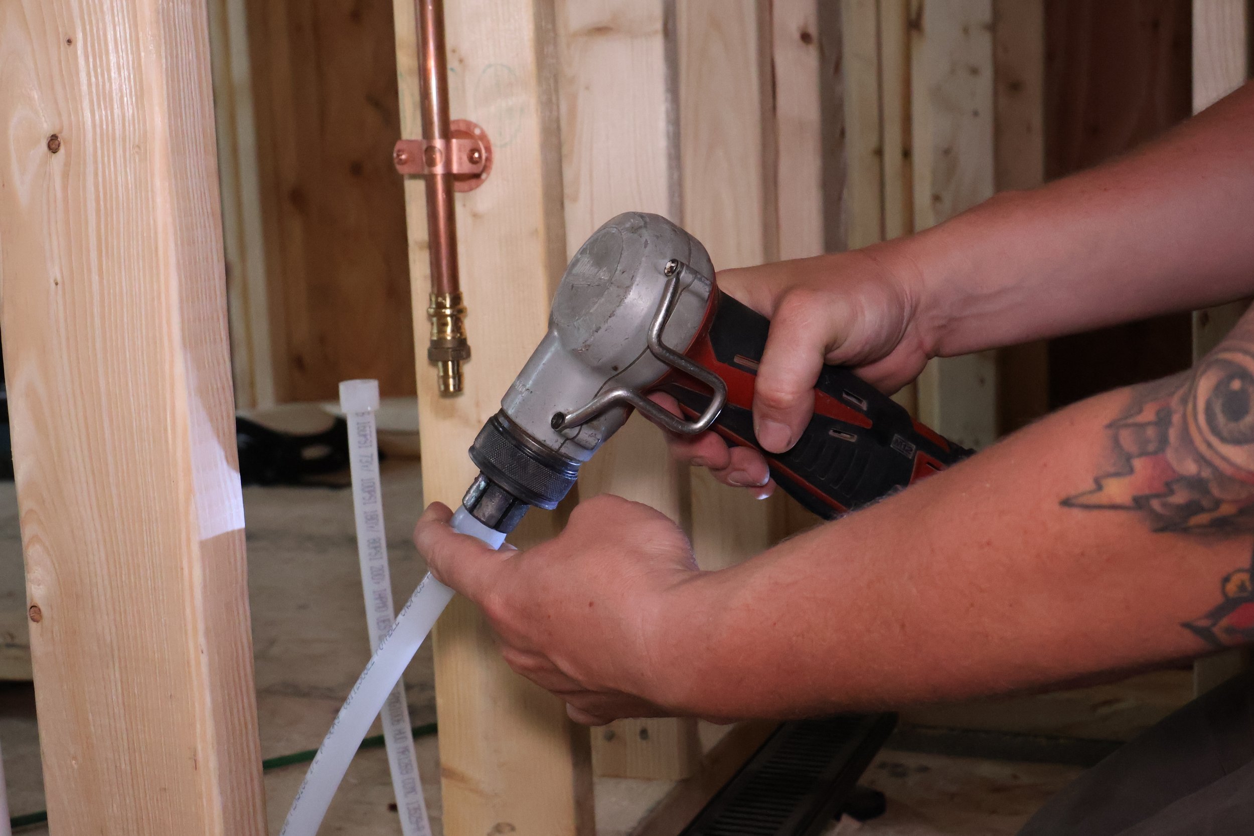 Person using a power drill on a PVC pipe in a construction site with wooden framing.
