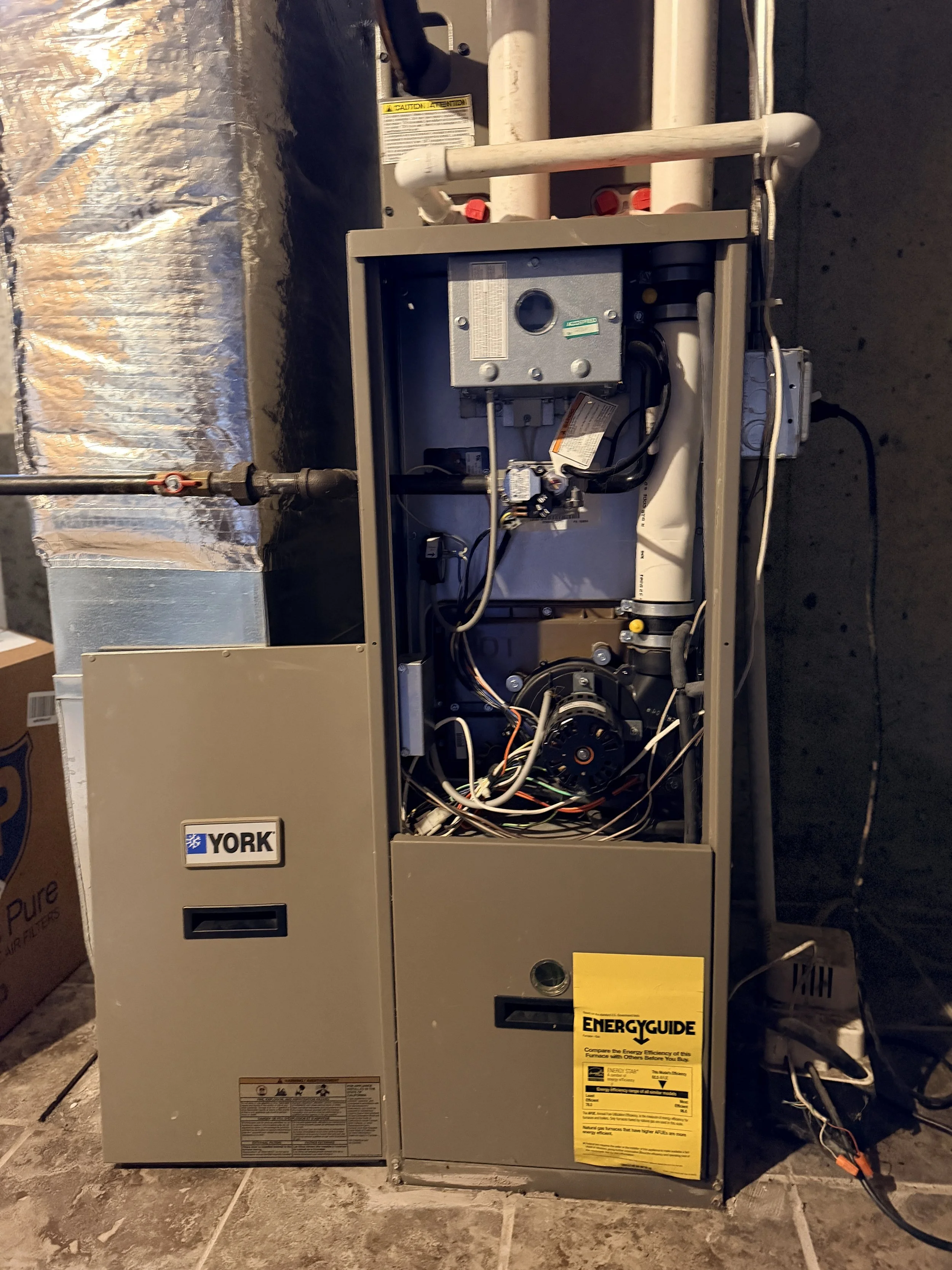 Interior of HVAC furnace unit showing wiring, fan motor, and ductwork with insulation.