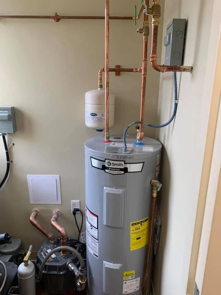 A water heater connected to copper pipes, a water filter mounted on the wall, and electrical wiring inside a utility room.