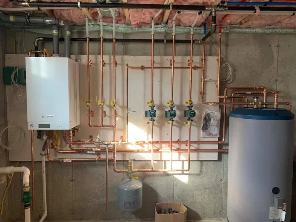 Underground boiler and plumbing system with copper pipes, water heater, and control units in a basement.