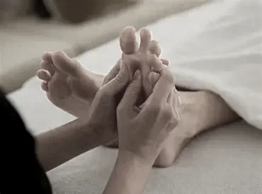 Close-up of hands giving a foot massage to someone lying down.
