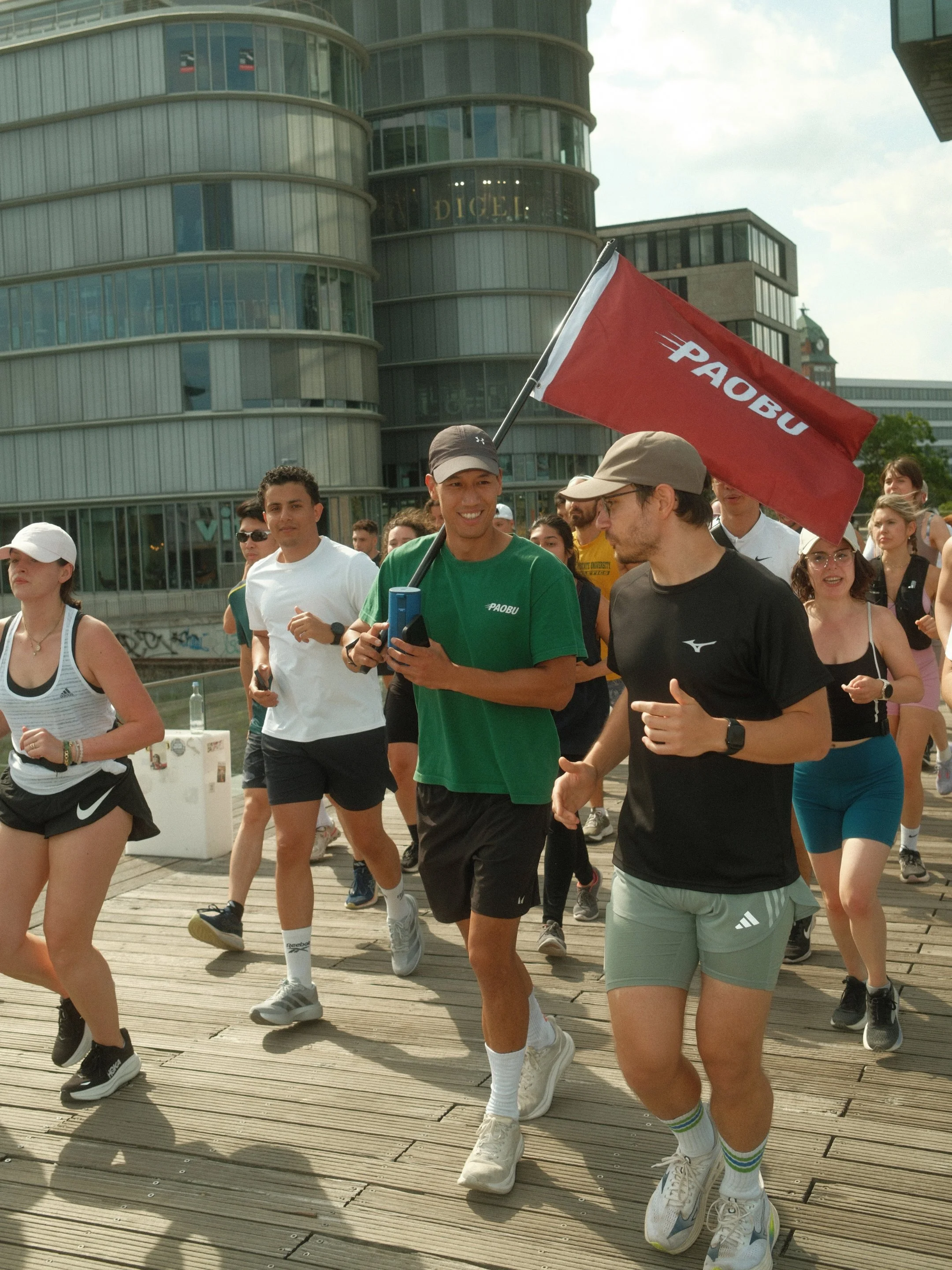 Menschen nehmen an einem Lauf-Event teil, einige tragen sportliche Kleidung, einige halten Wasserflaschen und einen roten PAOBU-Flagge.