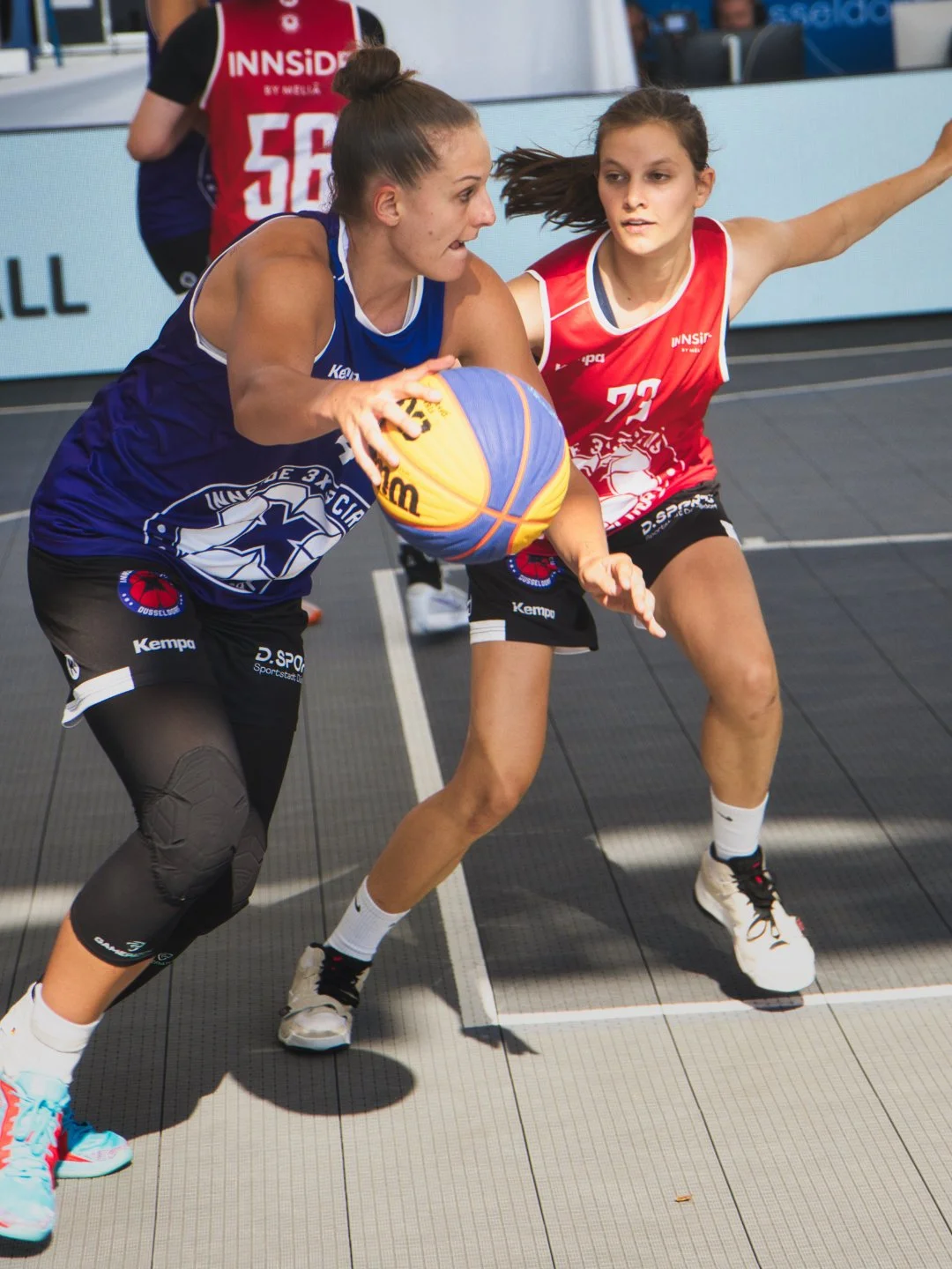Zwei Frauen spielen Basketball auf einem Basketballfeld, eine trägt ein blaues Trikot und die andere ein rotes Trikot, und sie konkurrieren um den Ball
