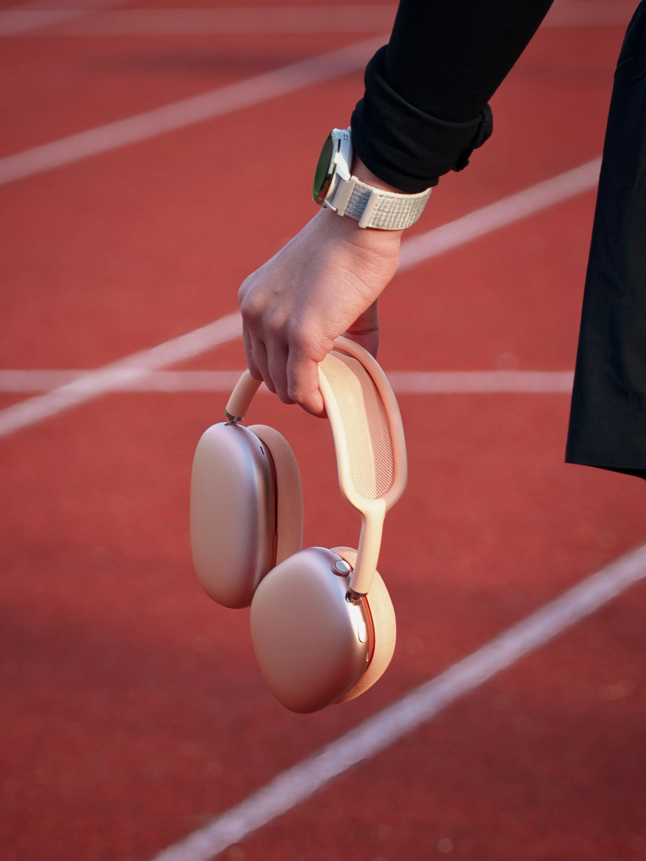 Nahaufnahme von einem Handgelenk mit einer Smartwatch, die auf einer roten Laufbahn liegt, während eine Person schwarze Sportkleidung trägt
