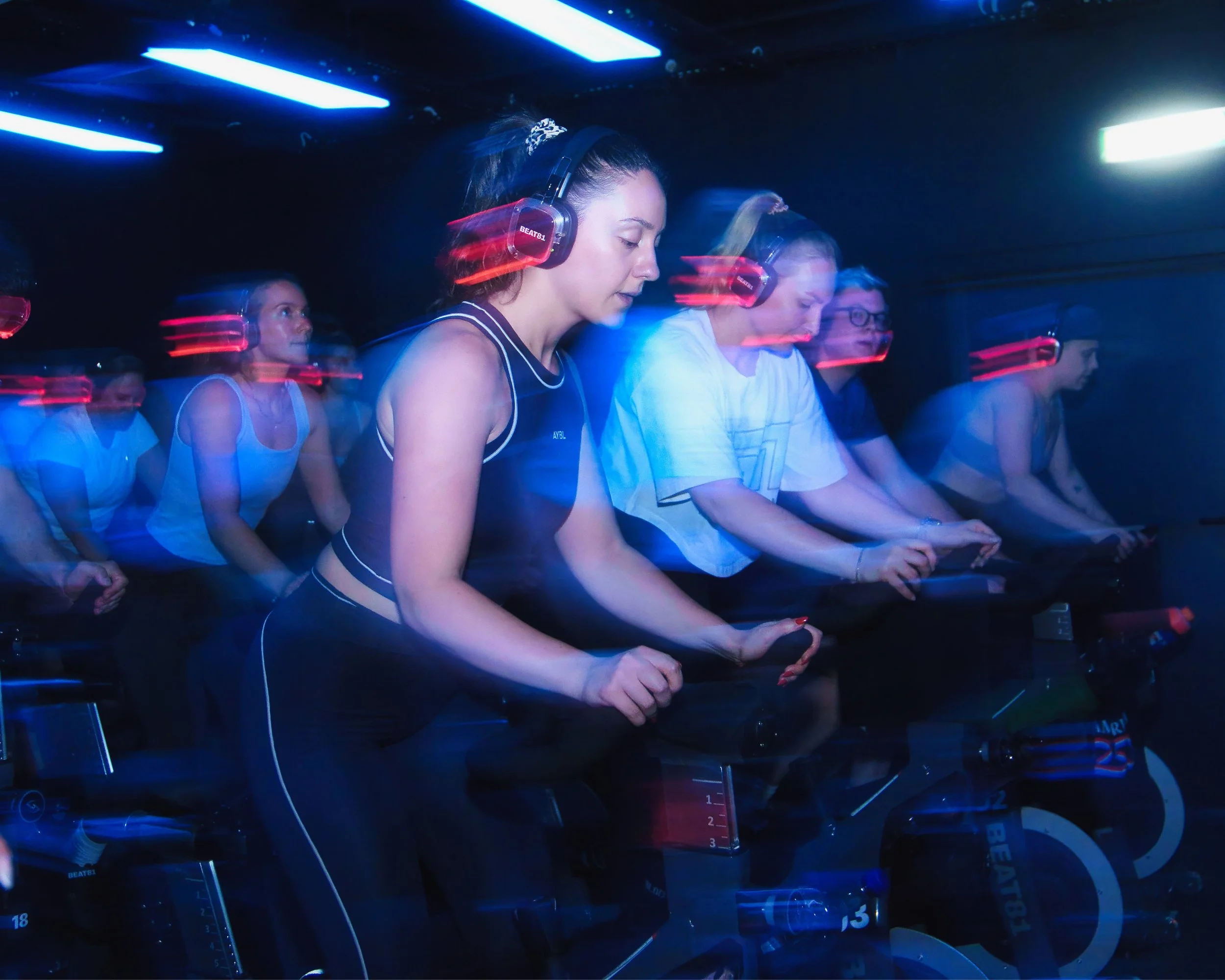 Menschen in einer dunklen Umgebung tragen Kopfhörer und sitzen mit ihren Händen auf Tastaturen, vermutlich in einem DJ- oder Musikproduktionsstudio, mit blauer und roter Beleuchtung