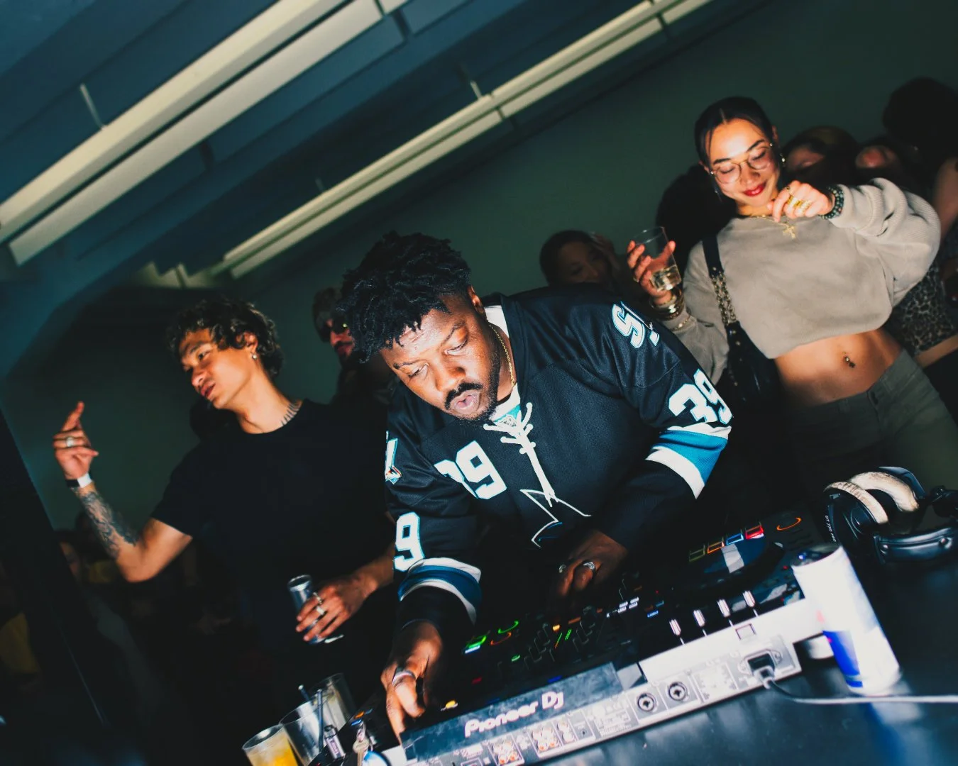 DJ mit Kopfhörern und Mixer, umgeben von Partygästen