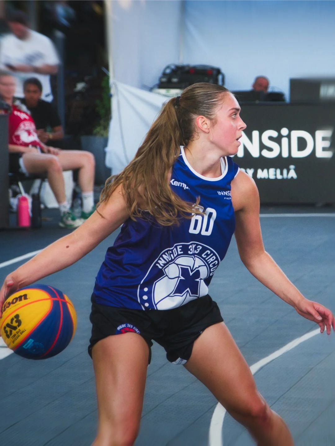 Eine weibliche Basketballspielerin in blauer Weste und schwarzen Shorts, die mit einem Basketball spielt