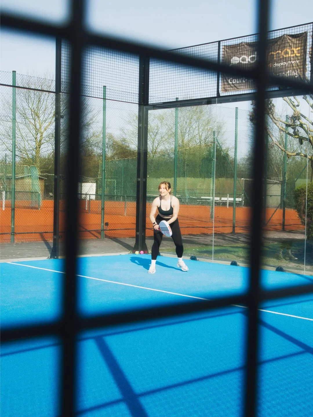 Frau spielt Padel auf einem Außenplatz, aufgenommen durch ein Gitter