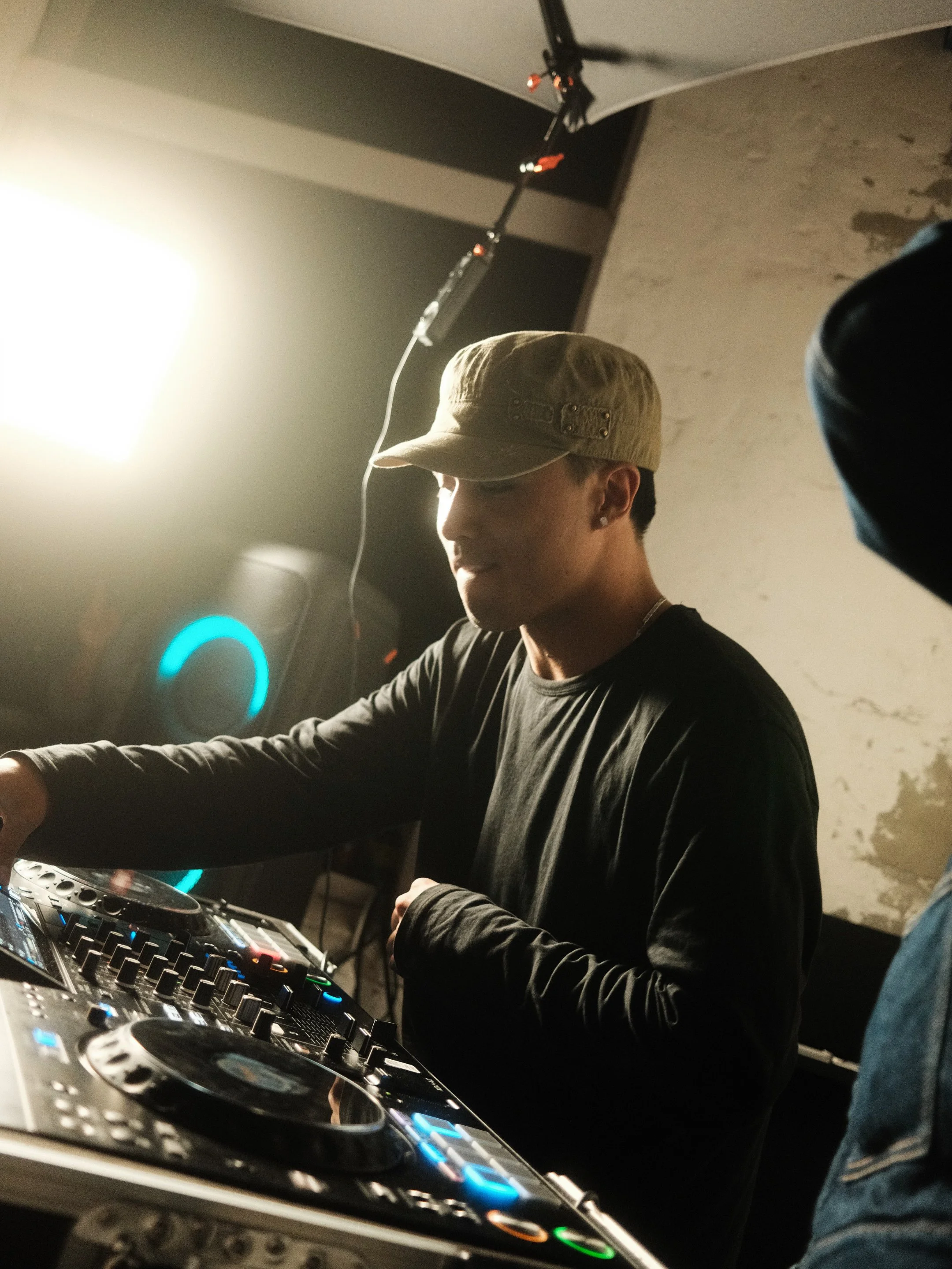 Ein junger Mann mit Kappe, der in einem Club auflegt, ist neben einem DJ-Pult